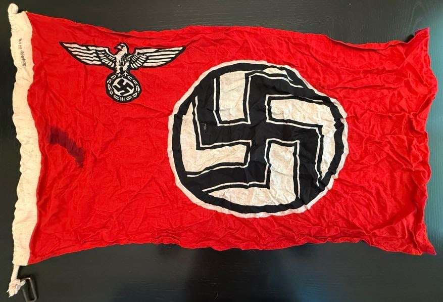 WWII German NSDAP Banner with Eagle Emblem Variant: This red banner displays the central white roundel and black swastika emblem associated with the National Socialist German Workers’ Party (NSDAP), accompanied by a smaller eagle insignia positioned