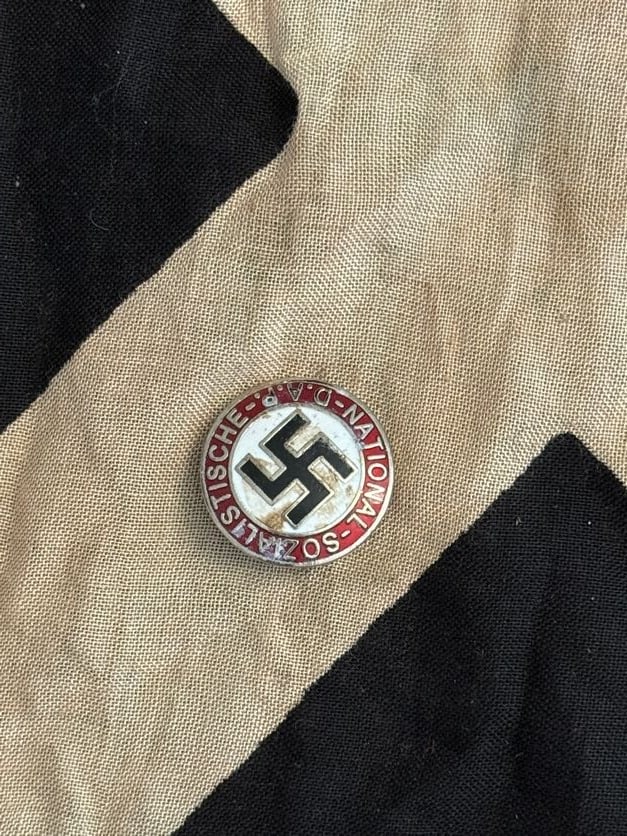 World War II German NSDAP Party Membership Badge (Enamel Pin): This circular enamel badge displays the inscription “Nationalsozialistische D.A.P.” encircling a central swastika on a white field, set against a red background. Worn by members of the Nationa