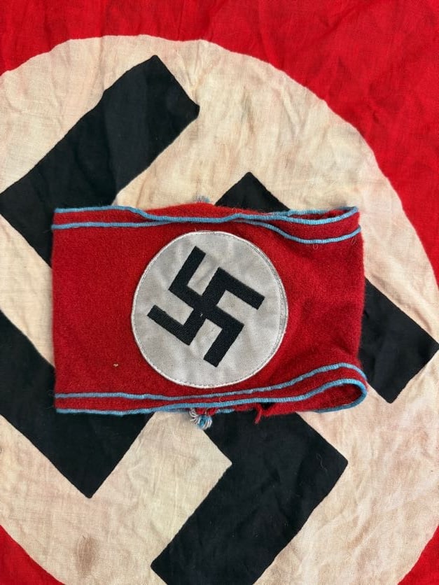 WWII German Political Armband with Light Blue Piping: This red wool armband features a white roundel with black swastika and distinctive light blue piping along the edges, indicating use by a specific political or administrative branch within the Nazi Pa
