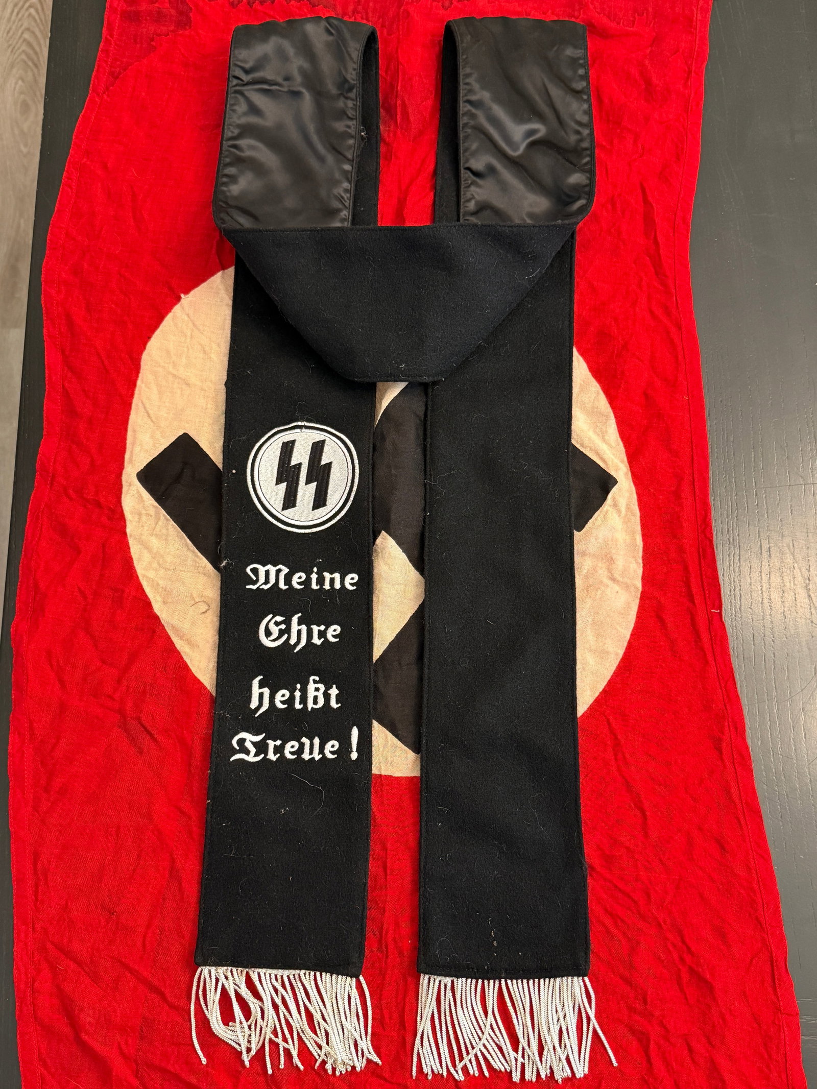 WWII German SS Ceremonial Sash with Motto “Meine Ehre heißt Treue?? (RZM Marked): This black ceremonial sash bears the SS insignia and the embroidered motto “Meine Ehre heißt Treue”, a phrase central to the identity of the Schutzstaffel (SS). The sash is constructed of bla