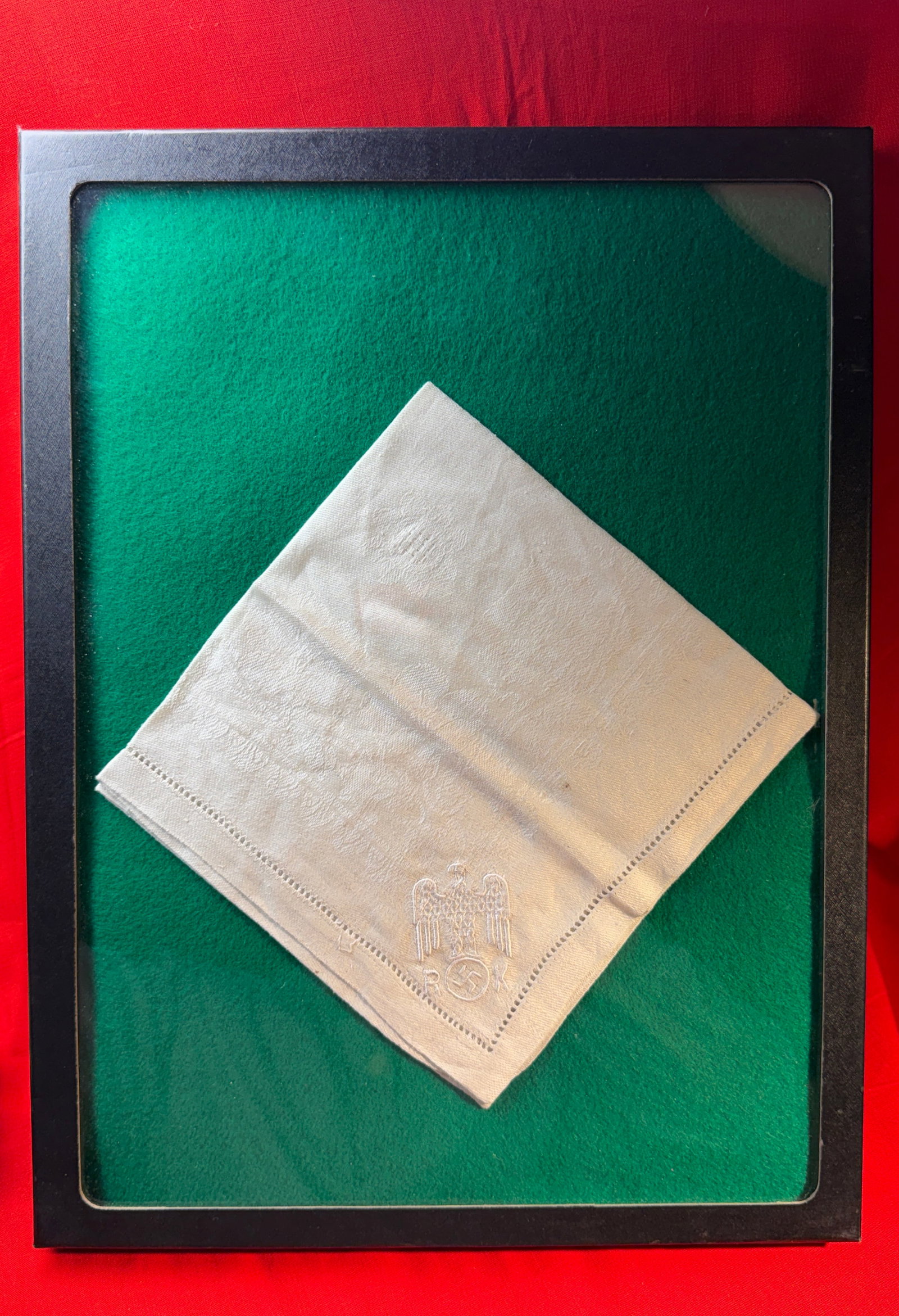 WW2 German Table Napkin with Reichsadler and “R.K.?? Monogram, c. 1933–1945: This linen table napkin bears a finely embroidered Reichsadler (imperial eagle) clutching a wreath, beneath which appears the monogram “R.K.” (Reichskanzlei). Executed in white thread on a whi