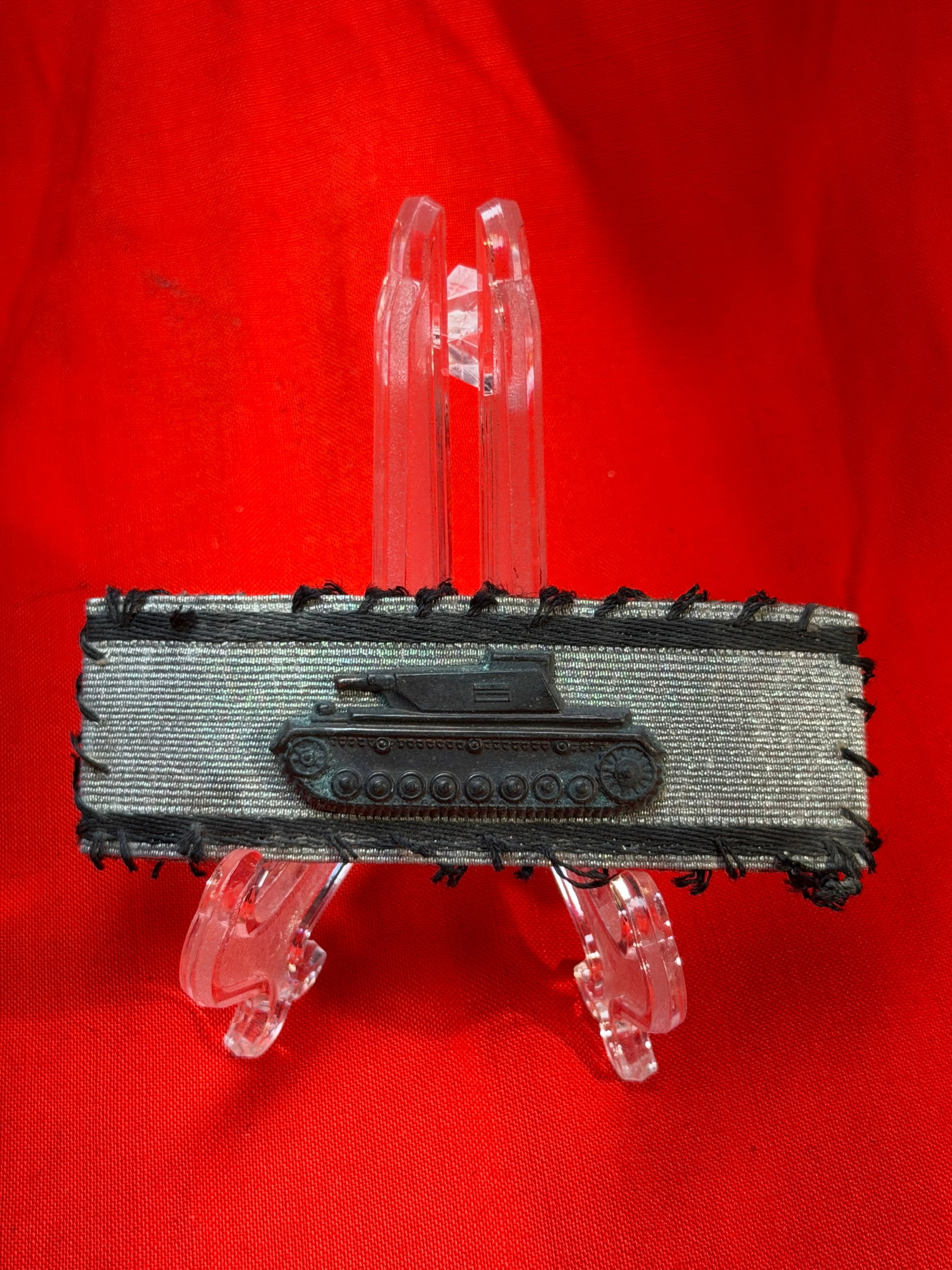 Armored Assault Badge (Panzerkampfabzeichen), WW2 Germany, c. 1939–1945: This cloth-mounted insignia features a miniature tank device affixed to a field-gray textile backing, bordered with dark stitching. The tank, rendered in metal, symbolizes Germany’s armored forces (