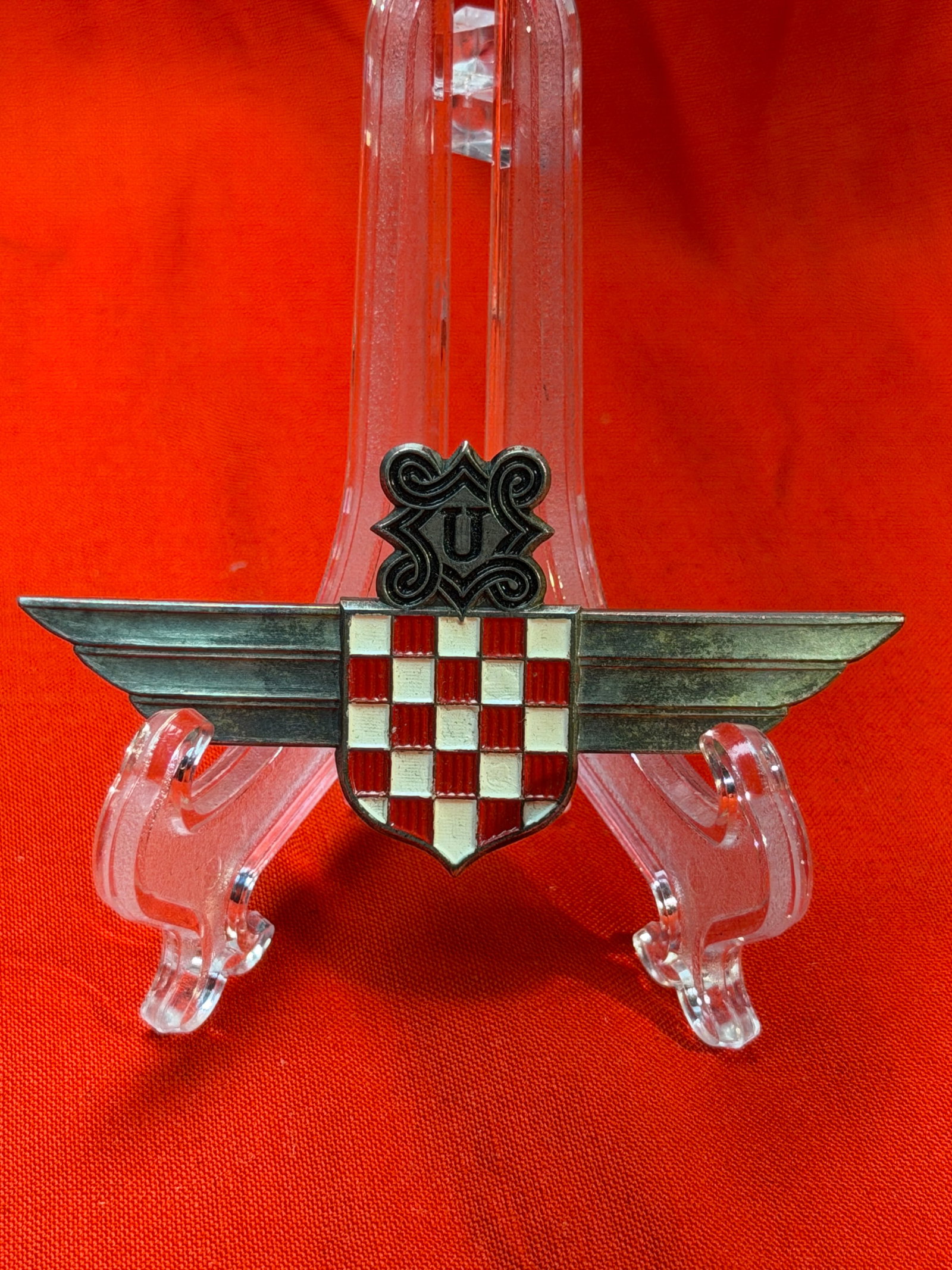WWII German Croatian Legion Air Force Badge – C.E. Juncker Berlin: WWII-era Croatian Legion / Air Force style badge, featuring a striking red and white checkerboard shield (Croatian coat of arms) set over a pair of outstretched wings. At the top is a decorative carto