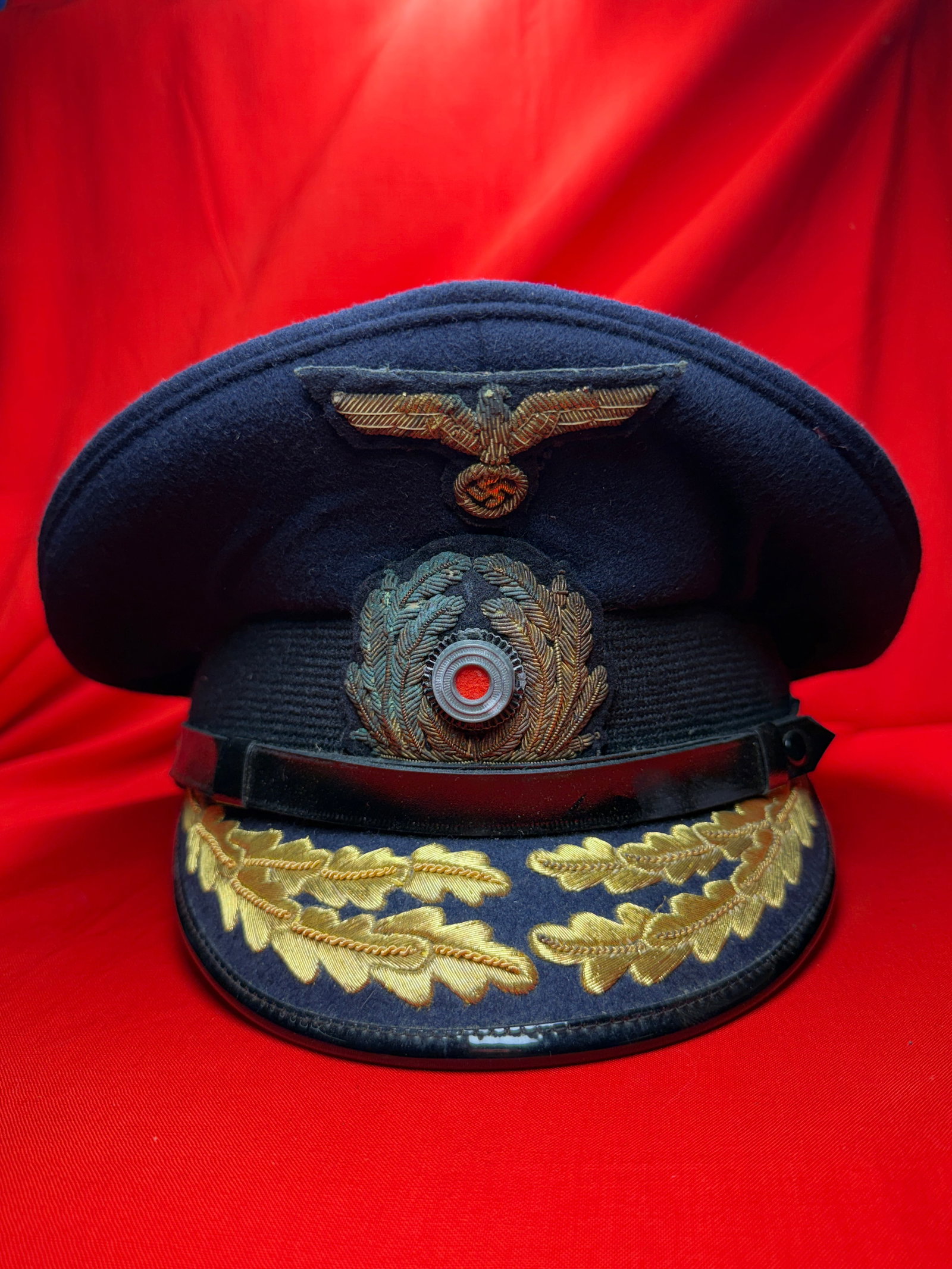 WWII German Kriegsmarine Officer Visor Cap (Schirmmütze) – Bullion Insignia, Oakleaf Visor: WWII German Kriegsmarine (Navy) officer visor cap (Schirmmütze), constructed in dark navy-blue wool with a classic saddle-form crown. The cap features a gold bullion Kriegsmarine-style eagle above a