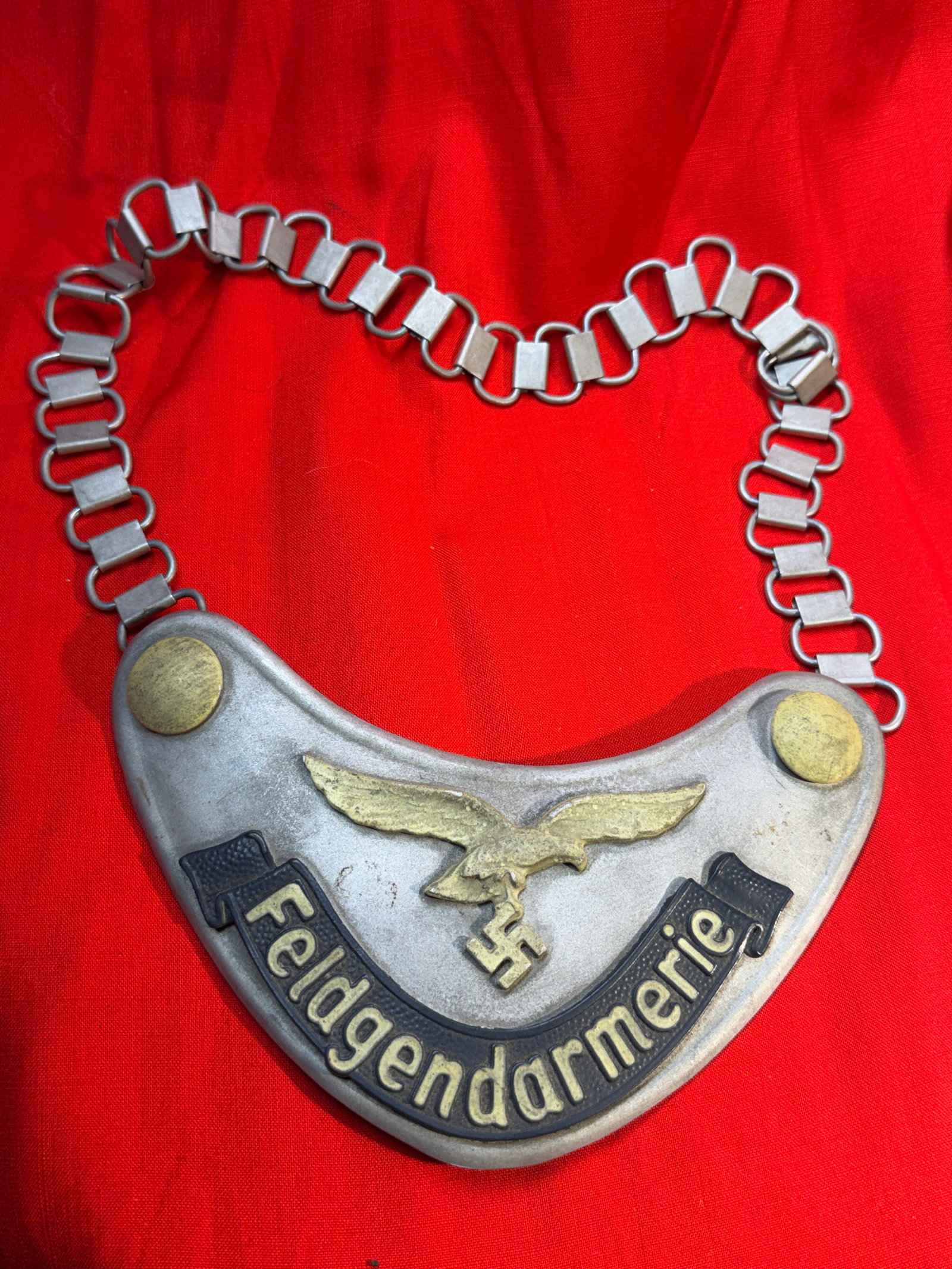 WW2 German Feldgendarmerie Gorget (Military Police Neck Plate) – D.R.G.M Marked: German Feldgendarmerie gorget, a distinctive metal neck plate worn by military police during the Second World War. This example features the classic crescent-shaped aluminum plate with applied brass e