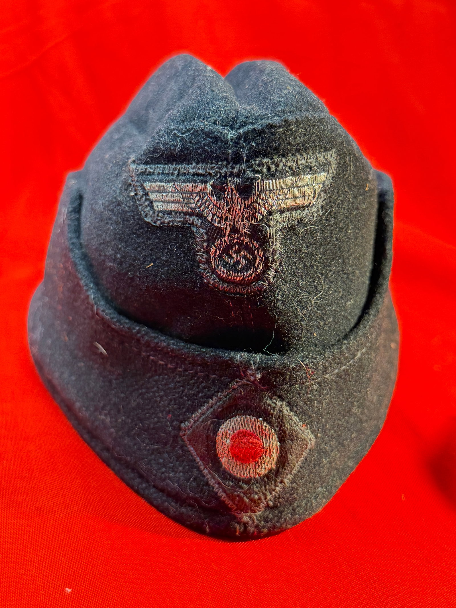 WW2 German Panzer Overseas Cap with Eagle Insignia and Cockade - Maker Marked: This black wool Panzer overseas cap features a fold-over side cap design with an embroidered eagle insignia positioned above a circular cockade in red, white, and black on the front. The exterior show
