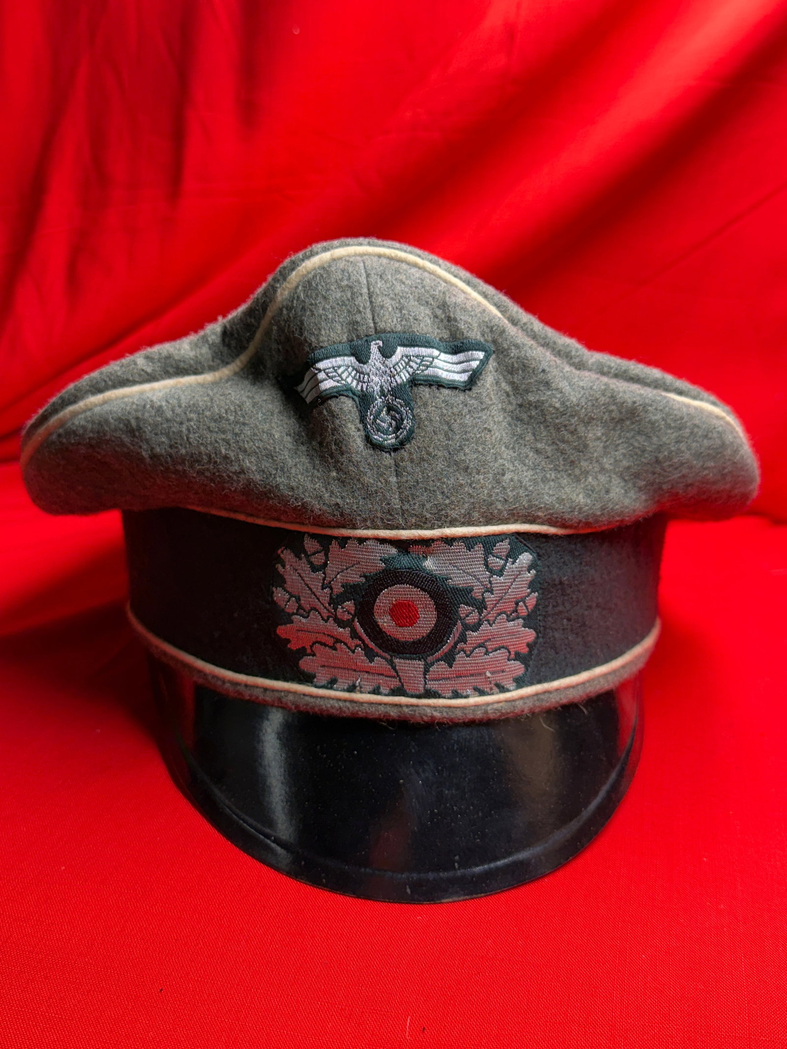 WW2 German Heer NCO/Officer Crusher Visor Cap: This crusher-style visor cap is made from field-gray wool with light-colored piping along the crown and band, reflecting a style commonly associated with Heer NCO and officer ranks. The cap has a soft