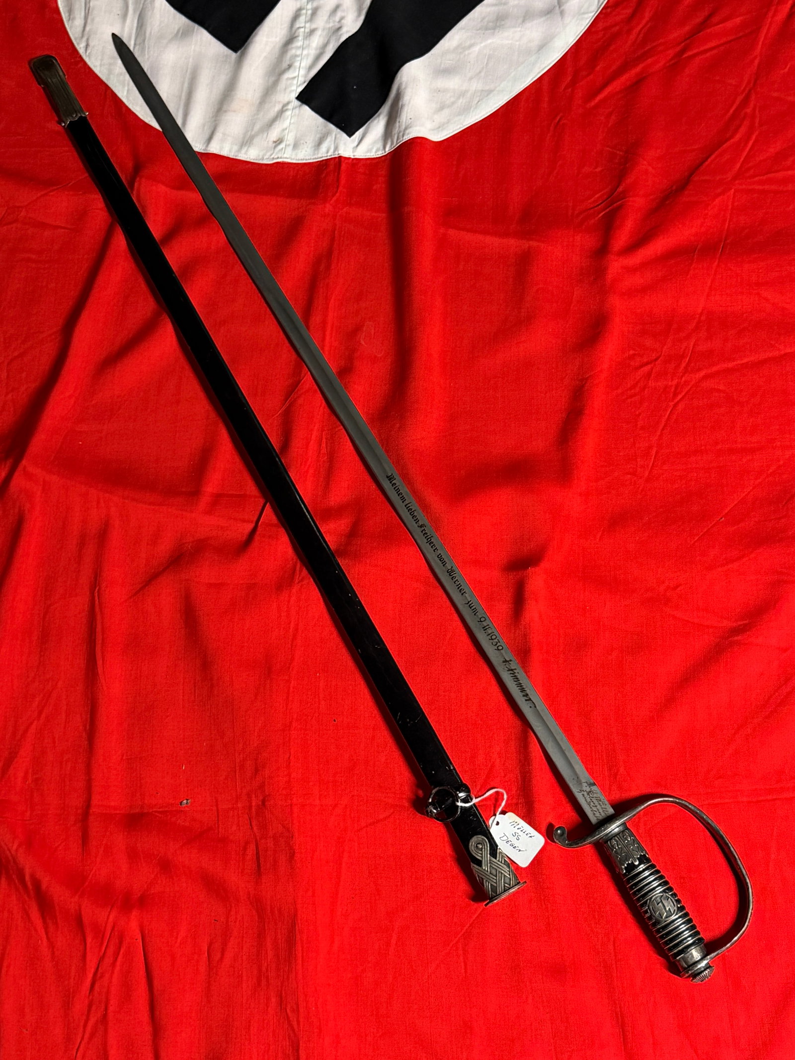 WW2 German Waffen SS Officer Damascus Blade Sword with Totenkopf Pommel and Etched Blade: This officer’s sword features a patterned Damascus blade with visible layered steel construction and etched inscriptions along the length, including “H. Himmler,” a 1939 date, and the phrase