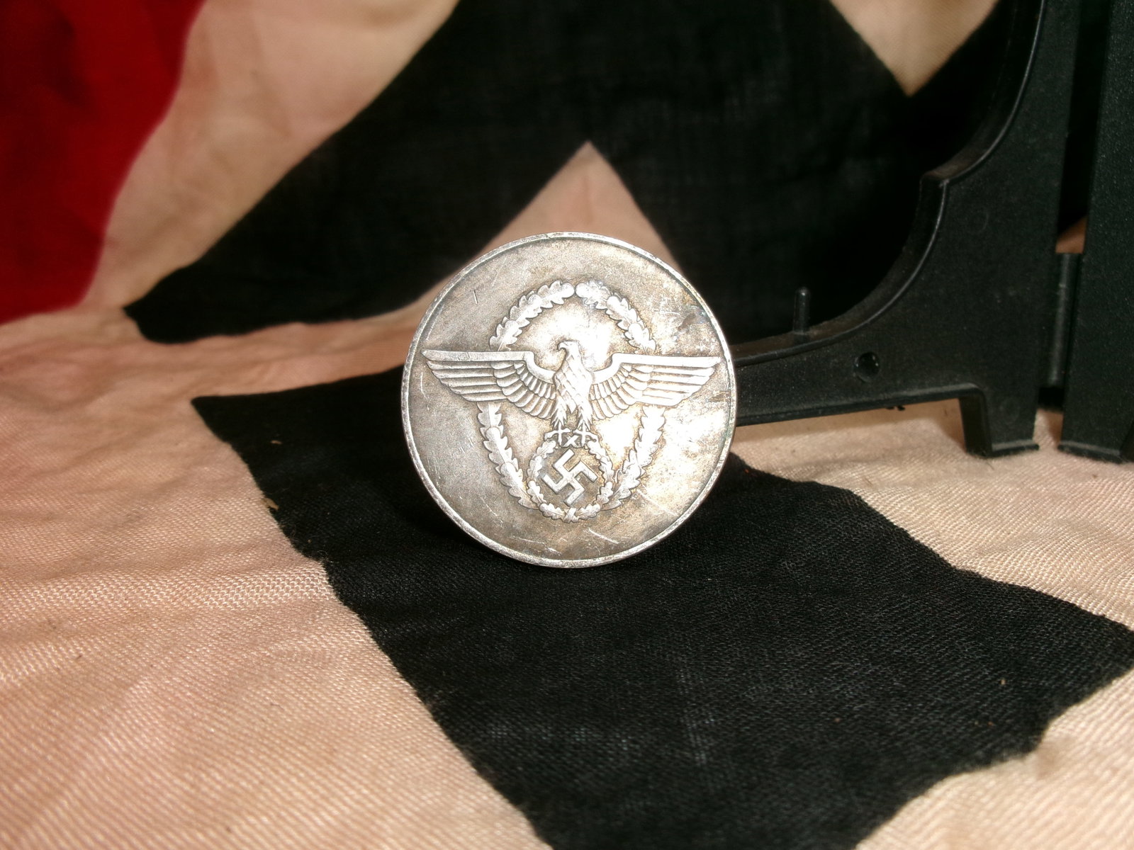 WWII German Police Long-Service Medal (8-Year Service Award): This circular silver-toned medal displays a spread-winged eagle clutching a wreath encircling a swastika—an official state emblem used in Nazi Germany. The reverse side bears the inscription “Für