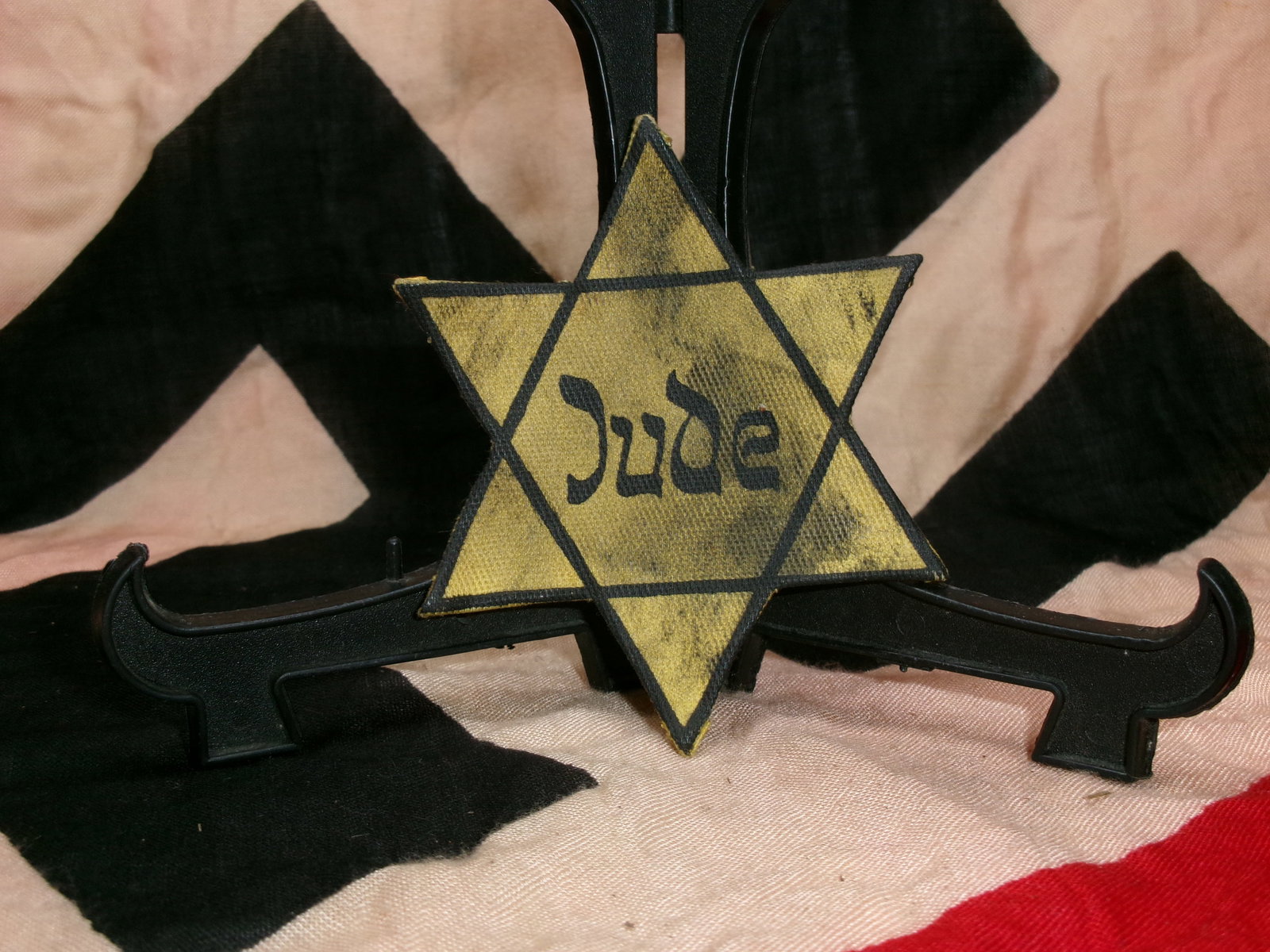 WWII Jewish Identification Badge (“Jude?? Star): A yellow Star of David badge marked with the word “Jude” (German for “Jew”) used in Nazi-occupied Europe during World War II. Beginning in 1941, Jewish people were forced to wear these