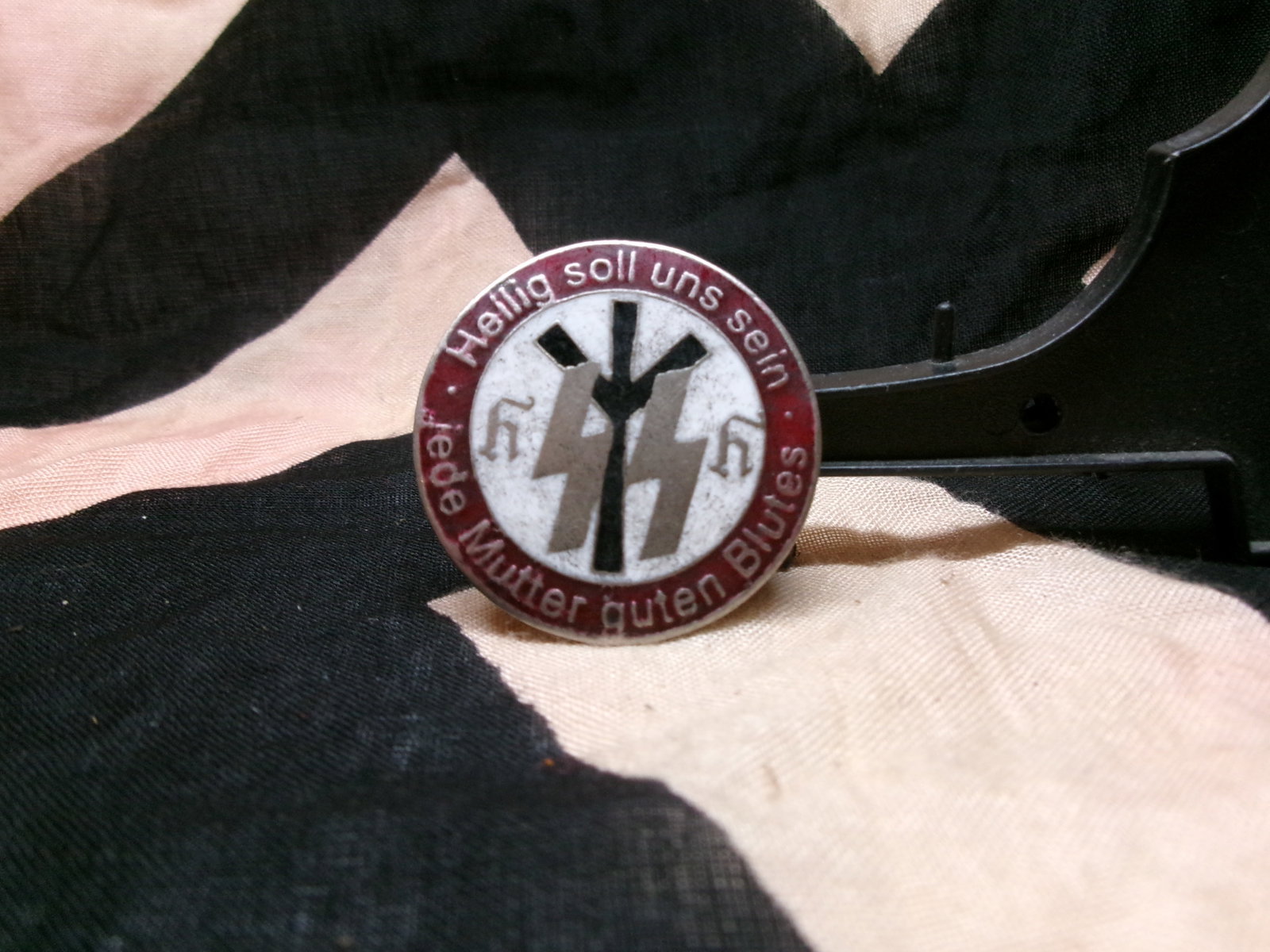 WWII SS Membership Lapel Pin (“Meine Ehre heißt Treue??) By Ges. Gesch.: A circular badge bearing the SS lightning-bolt insignia and the motto “Meine Ehre heißt Treue” (“My honor is loyalty”), associated with the Schutzstaffel (SS), an elite paramilitary o