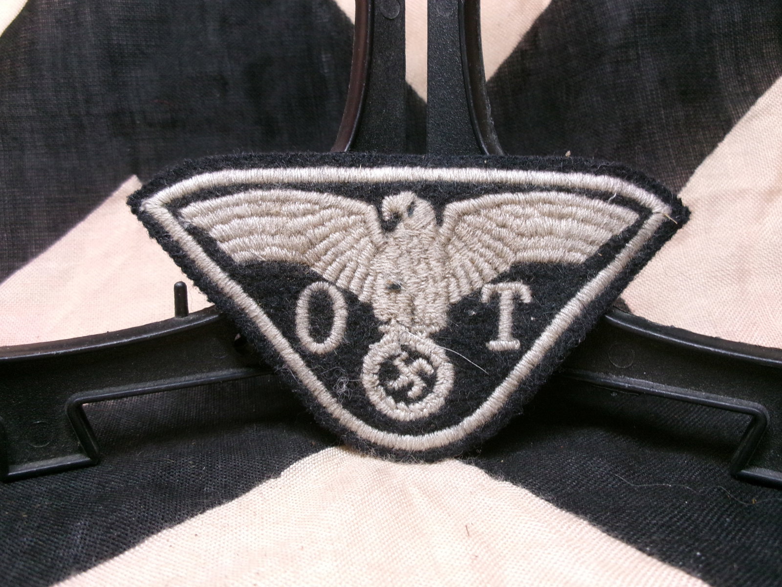 WWII German Organization Todt (OT) Qualification Badge: This triangular cloth patch features a German eagle above a wreath and swastika, with the numbers “0” and “1” flanking the design. Such insignia were typically worn likely for a female