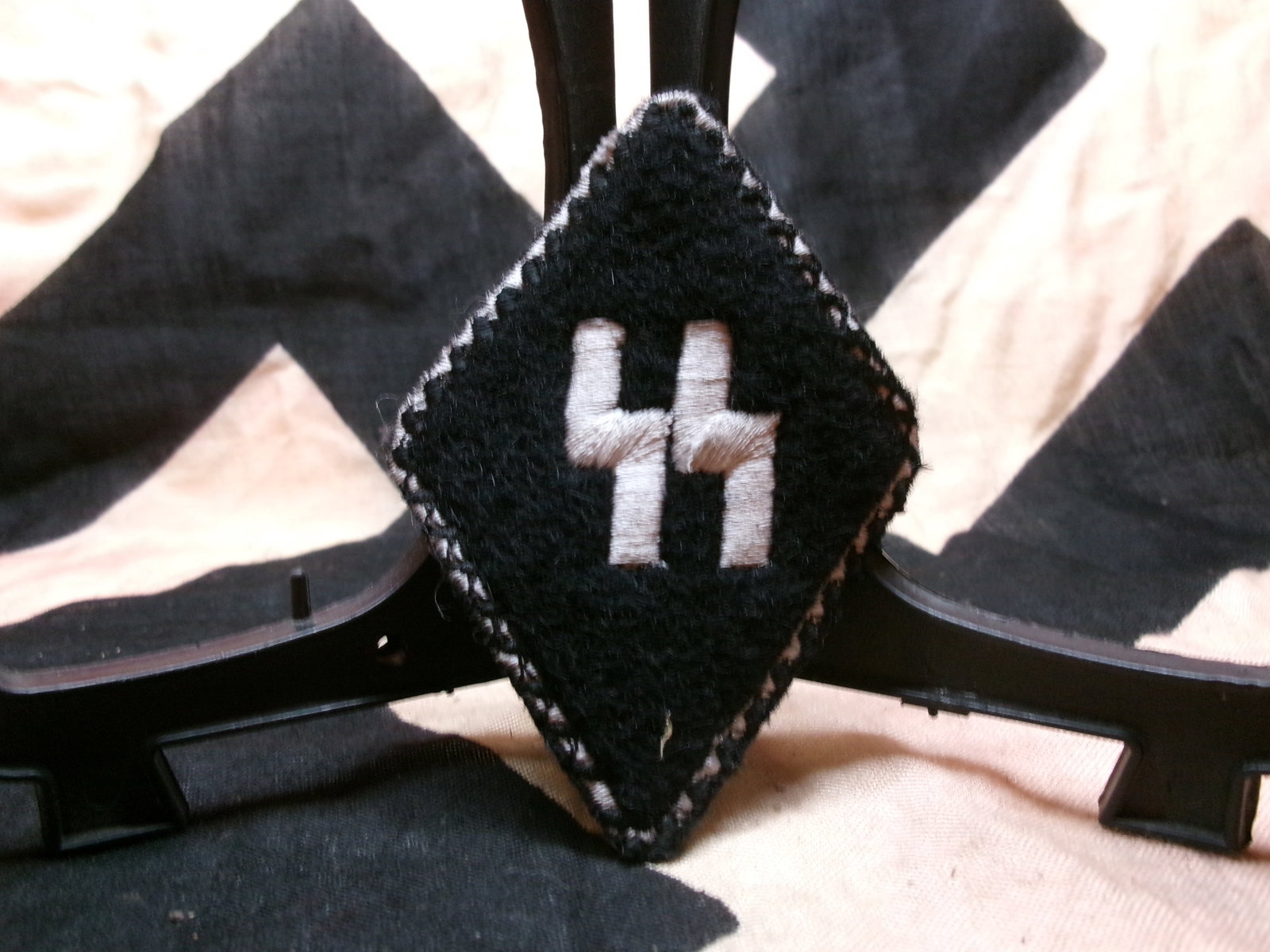 WWII Waffen-SS Collar Tab (Runic Insignia with RZM Tag): This black diamond-shaped cloth patch displays the SS runes embroidered in silver thread, worn as a collar tab on SS uniforms. The reverse includes an RZM (Reichszeugmeisterei) label, indicating offic