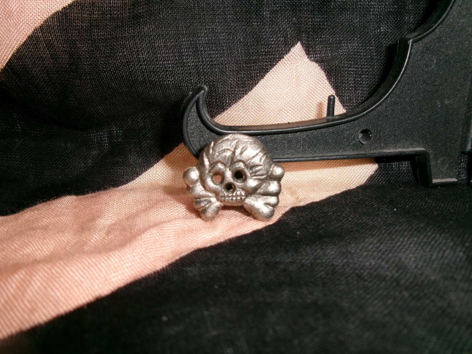 WWII German Totenkopf Collar Insignia (Metal Variant): This small metal skull-and-crossbones badge is a Totenkopf collar insignia, typically associated with SS units during World War II. Worn on the collar of uniforms, it functioned as a unit or branch id