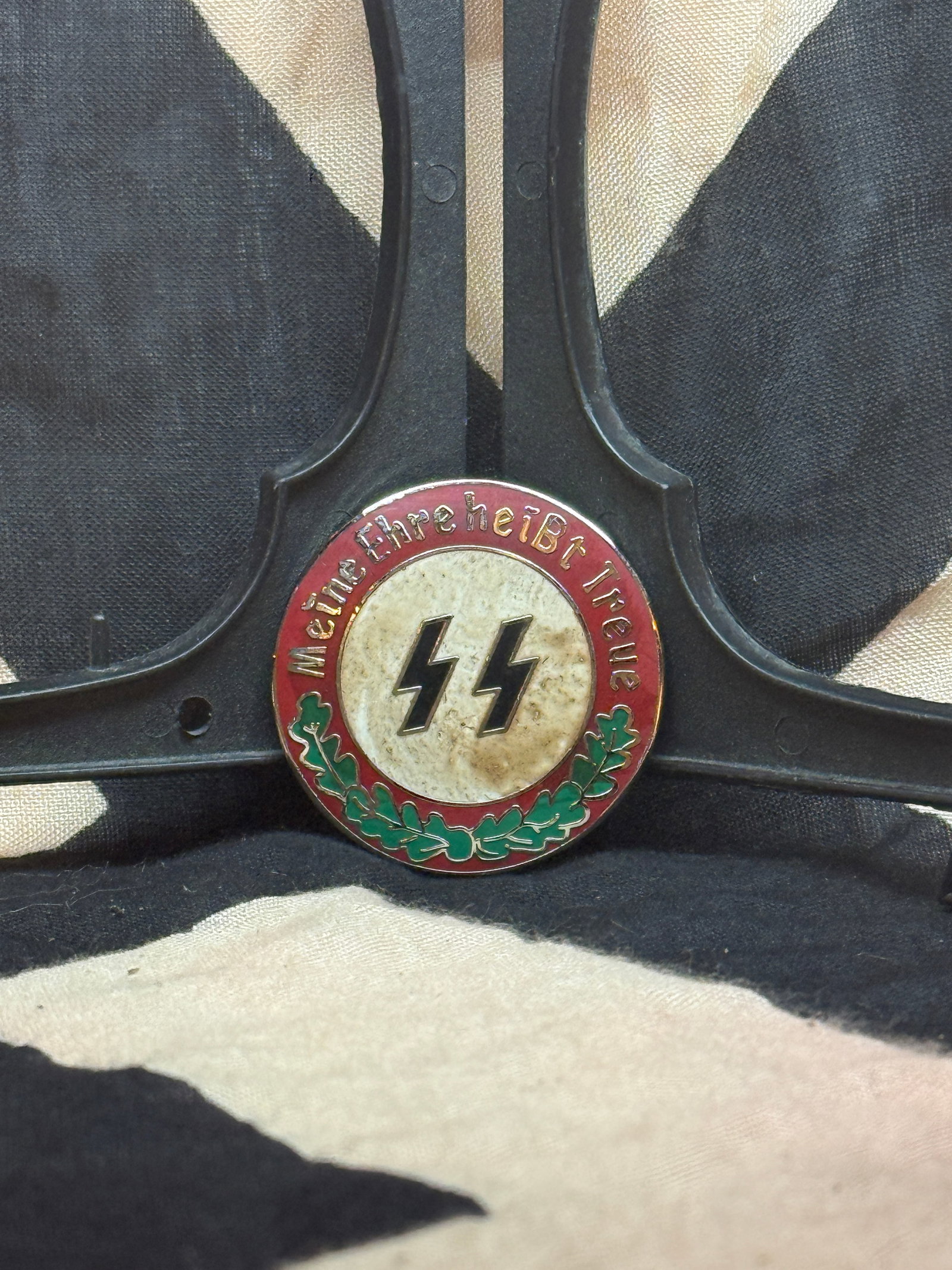 WWII German SS Membership/Commemorative Badge (“Meine Ehre heißt Treue??): This circular enamel badge bears the SS motto “Meine Ehre heißt Treue” (“My Honor is Loyalty”) encircling the SS runes. Featuring a red outer ring, white center, and green oak leaves,