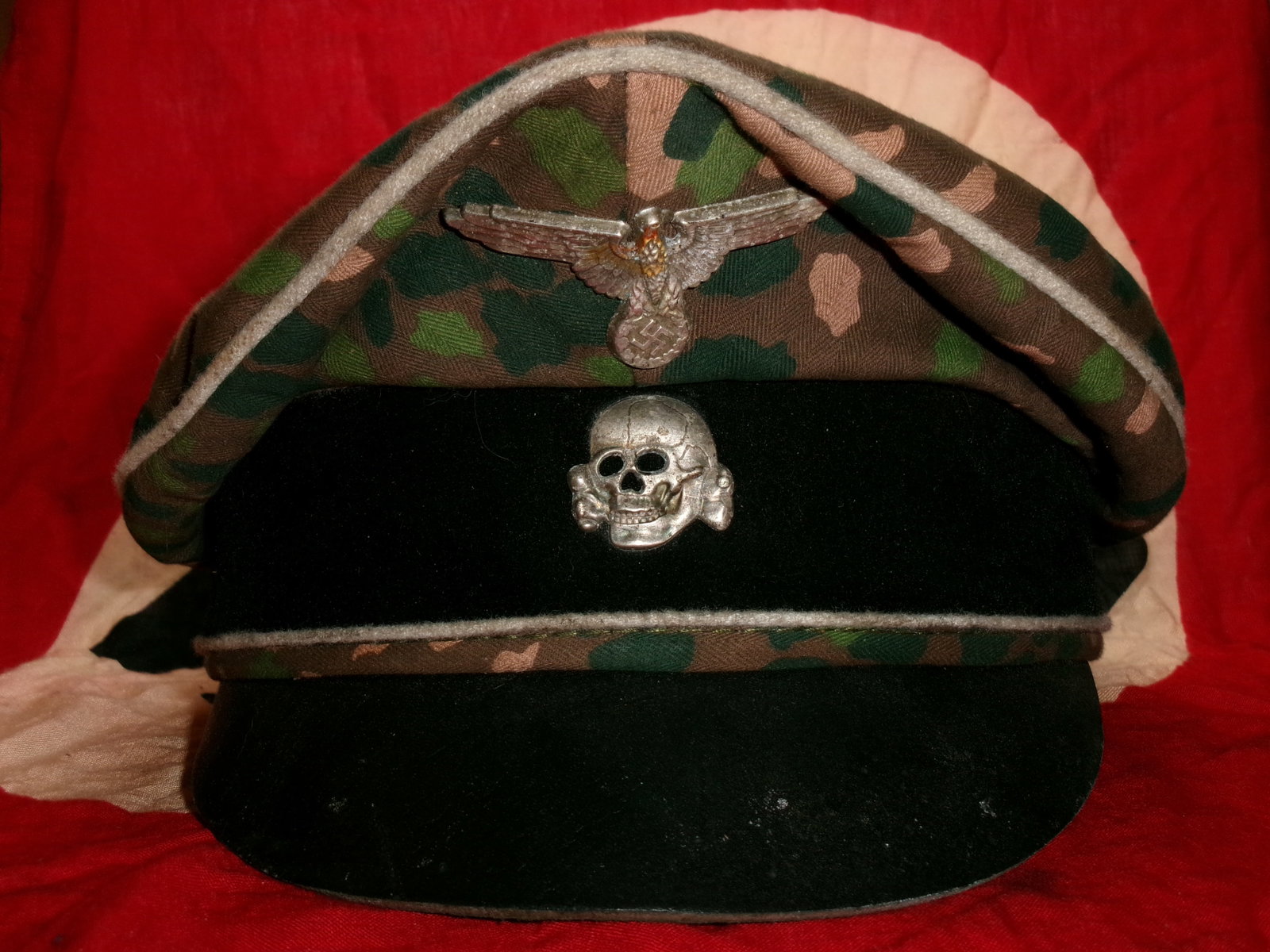 WWII Waffen-SS Camouflage Field Cap (M43 Style) with Insignia: This field cap is a camouflage-patterned example of the German M43 Einheitsfeldmütze, adapted here with Waffen-SS insignia. The cap displays a subdued, multi-tone camouflage fabric typical of late-wa
