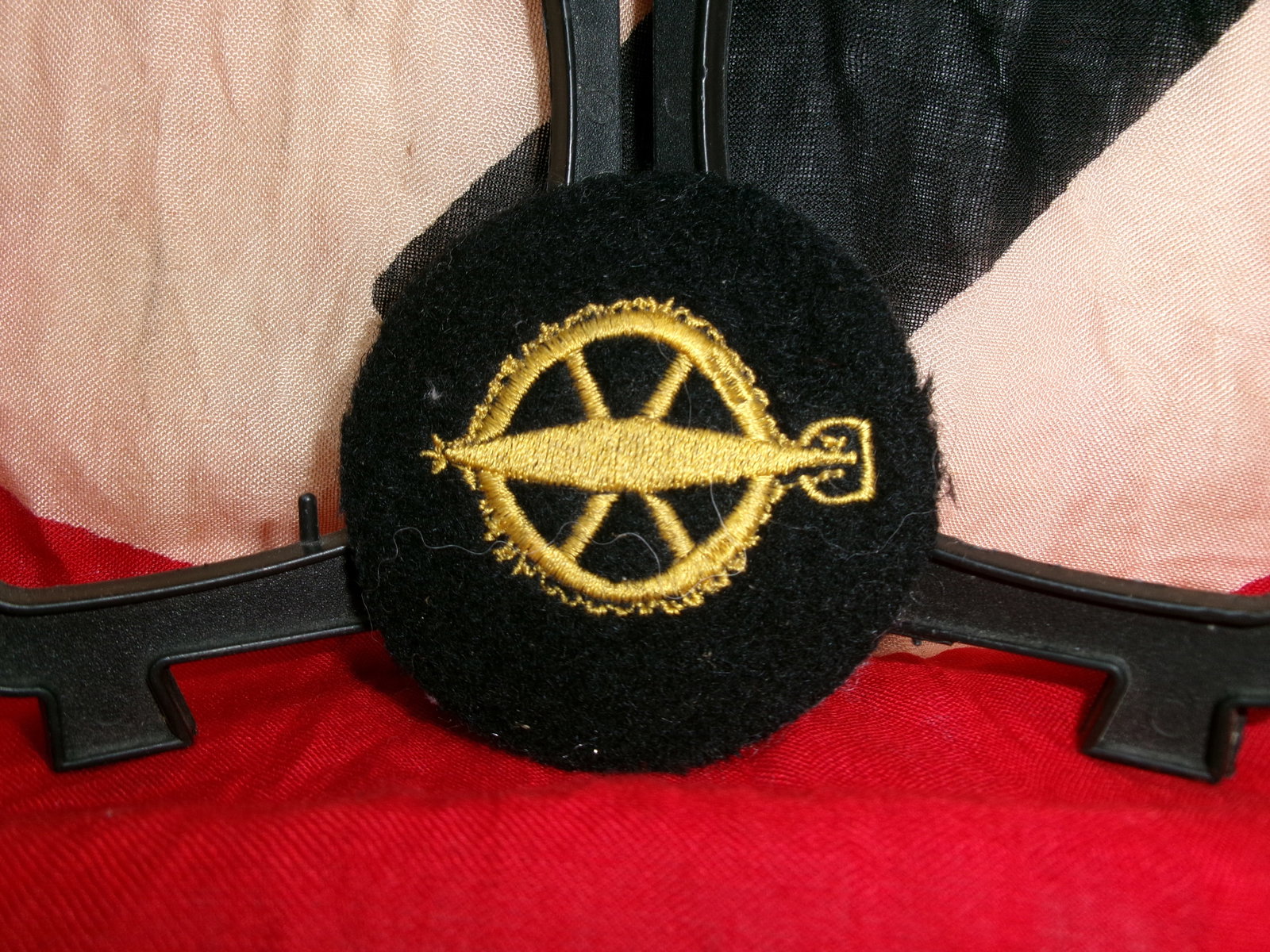 WWII German Artillery or Technical Trade Sleeve Insignia (Embroidered Specialist Badge): This circular black cloth insignia features a gold-embroidered wheel with a horizontal device resembling a cannon barrel or mechanical element. The wheel motif is traditionally associated with artille