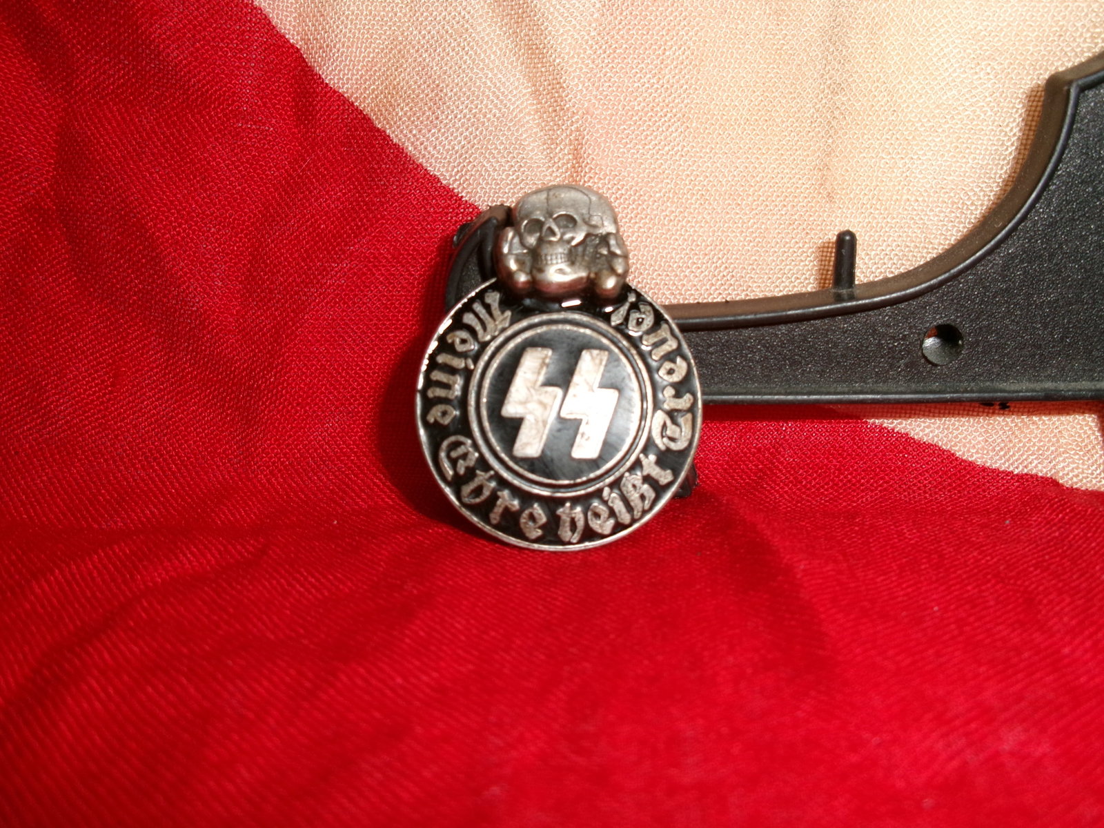 WWII German SS Membership Pin (Schutzstaffel Lapel Badge) By Ges. Gesch. RZM M13/42 SS: This small circular metal pin features the SS runes at its center, surrounded by the inscription “Meine Ehre heißt Treue” (“My honor is called loyalty”), the official motto of the Sch