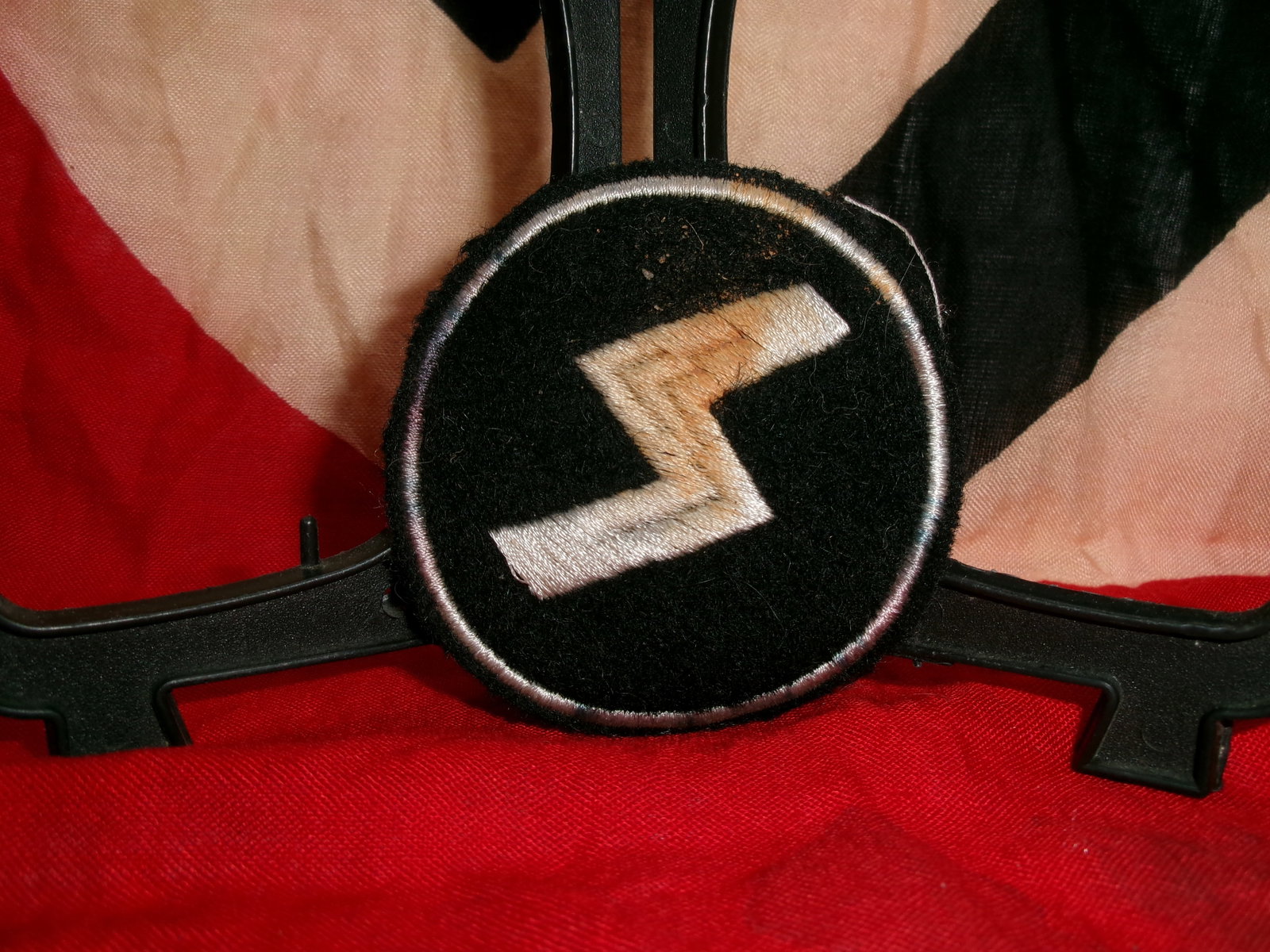 WWII German SS Sleeve Insignia (Runic “Sig?? Emblem Patch): This circular black cloth insignia features the distinctive double “Sig” runes embroidered in silver thread, emblematic of the Schutzstaffel (SS) during the Second World War. The runes, derive