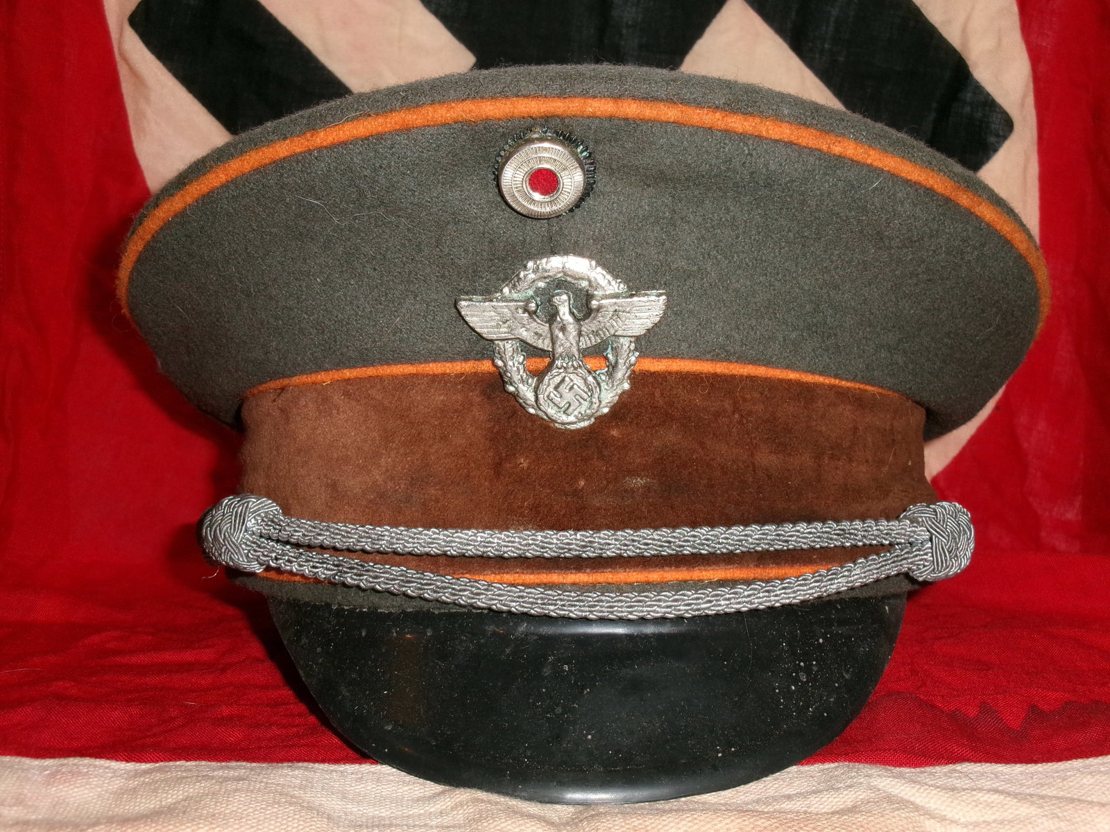 WWII German Political or Paramilitary Visor Cap (Brown Band with Orange Piping): This visor cap features a field-grey wool body, a brown velvet or cloth center band, and orange piping along the crown and band edges. The front is adorned with a metal eagle-and-wreath insignia and a