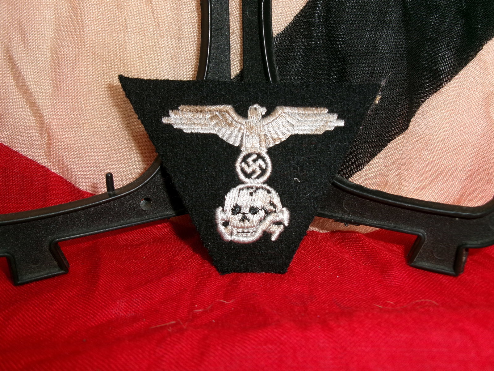 WWII Waffen-SS Style Sleeve Insignia with Eagle and Skull Motif: This triangular black cloth patch combines a national eagle above a skull (Totenkopf) motif, both associated with Waffen-SS symbolism during the Second World War. Authentic SS insignia were typically 