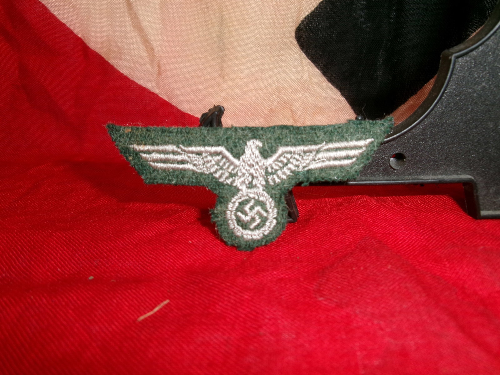 WWII German Army (Heer) Bevo Woven Breast Eagle (Green Backing): This cloth insignia is a Bevo-style machine-woven breast eagle used by the German Army (Heer) during World War II. The eagle, rendered in light gray thread, clutches a wreath enclosing a central emble