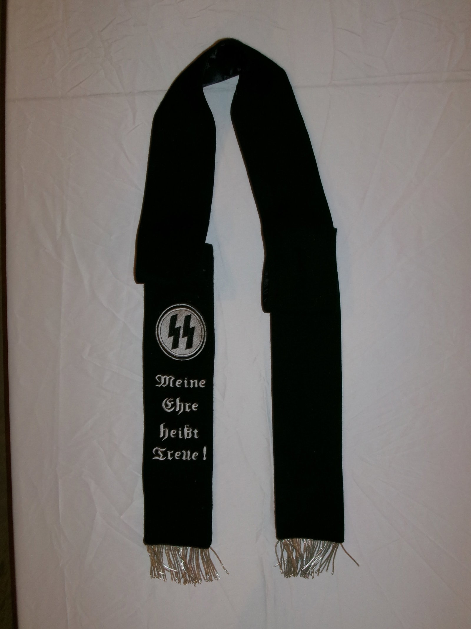WWII German Waffen-SS Motto Scarf (“Meine Ehre heißt Treue??): This black cloth scarf bears the Waffen-SS motto “Meine Ehre heißt Treue” (“My honor is loyalty”) embroidered in white thread, accompanied by the SS runic emblem within a circular dev