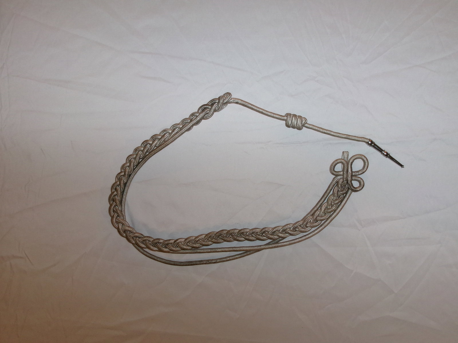 WWII German Officer’s Dress Aiguillette (Braided Shoulder Cord): This braided cord aiguillette is constructed from silver-toned thread and was worn as a decorative shoulder ornament on formal or dress uniforms. Featuring a looped fastening and metal-tipped ends, it
