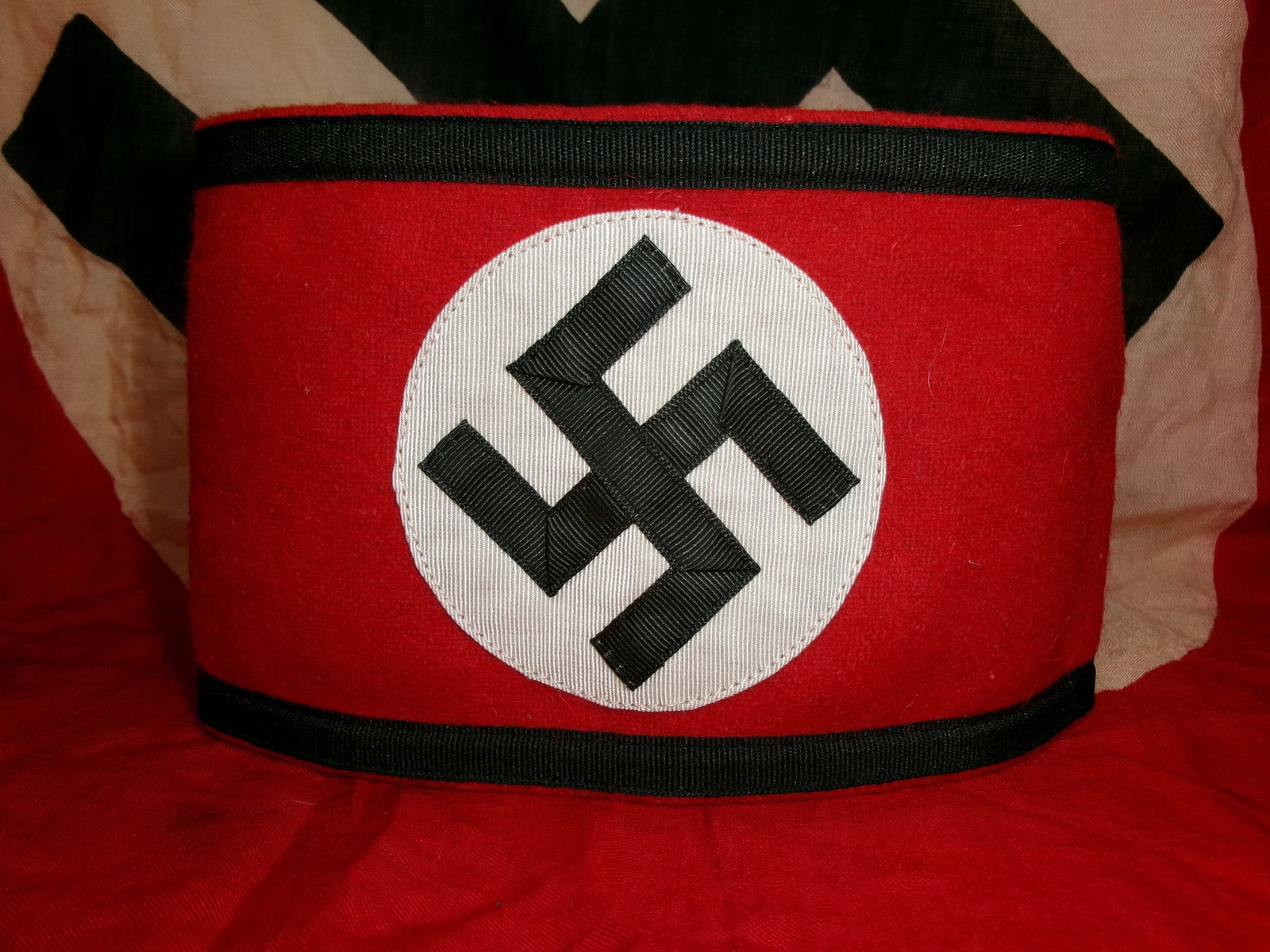 WWII Era German Waffen-SS Armband with RZM Cloth Tag: A red Waffen SS cloth armband featuring a white roundel with a black swastika, worn by members of the Waffen SS during World War II. The interior label indicates SS-associated manufacturing or distrib