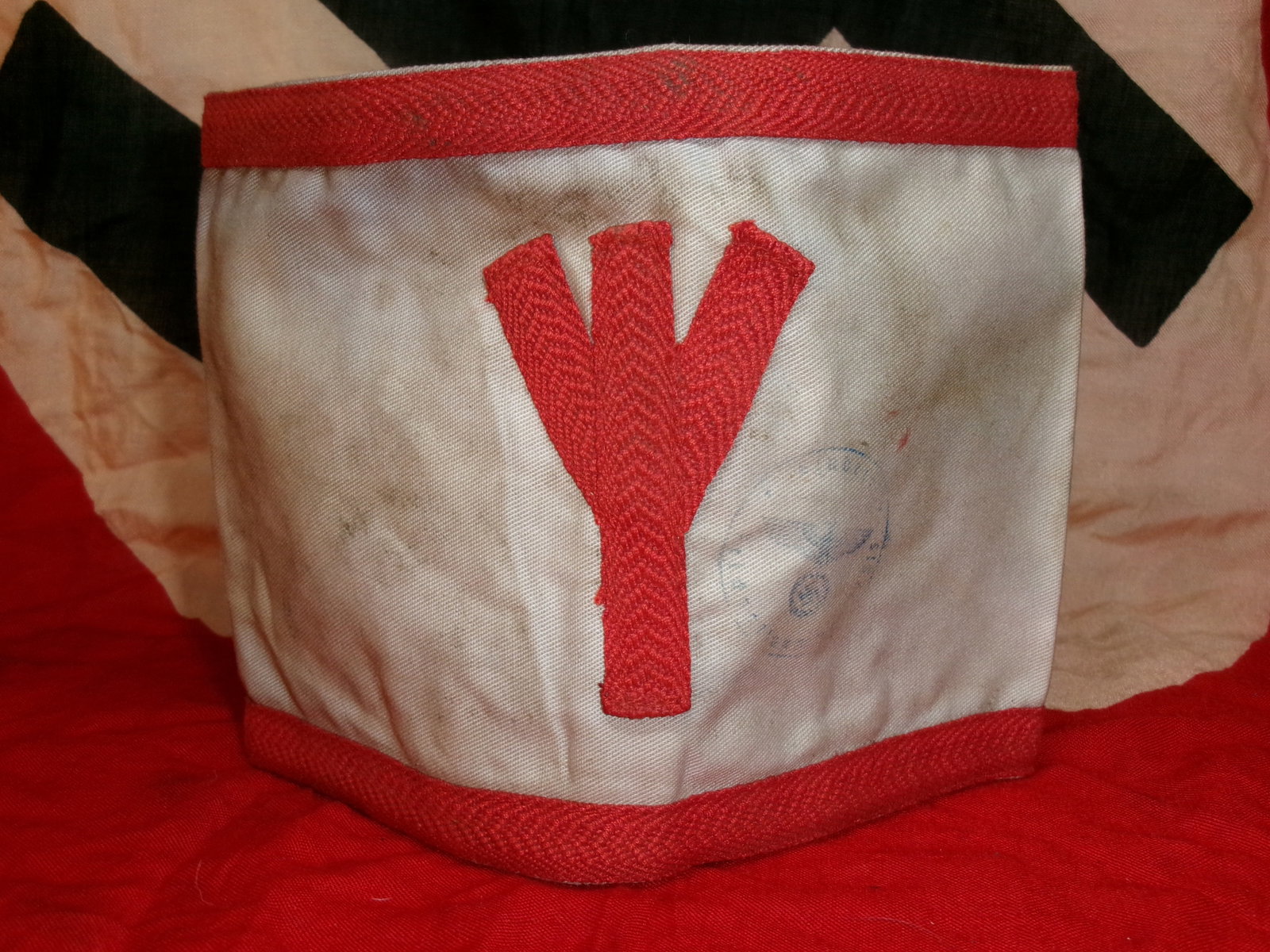WWII Hitler Youth (Hitlerjugend) Medical Armband With Inspection Stamp: A white cloth armband with red borders featuring a red “life rune” (Lebensrune), associated with medical or first-aid personnel within the Hitler Youth during World War II. Such armbands were 