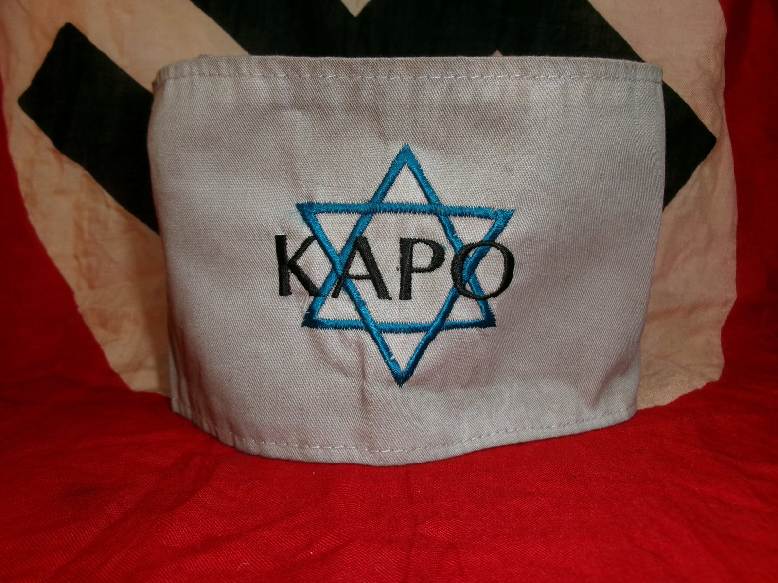 WWII Nazi Concentration Camp Prisoner Armband (“KAPO??): A white cloth armband marked with a blue Star of David and the word “KAPO,” identifying a prisoner functionary within Nazi concentration camps. Kapos were inmates assigned supervisory roles ov