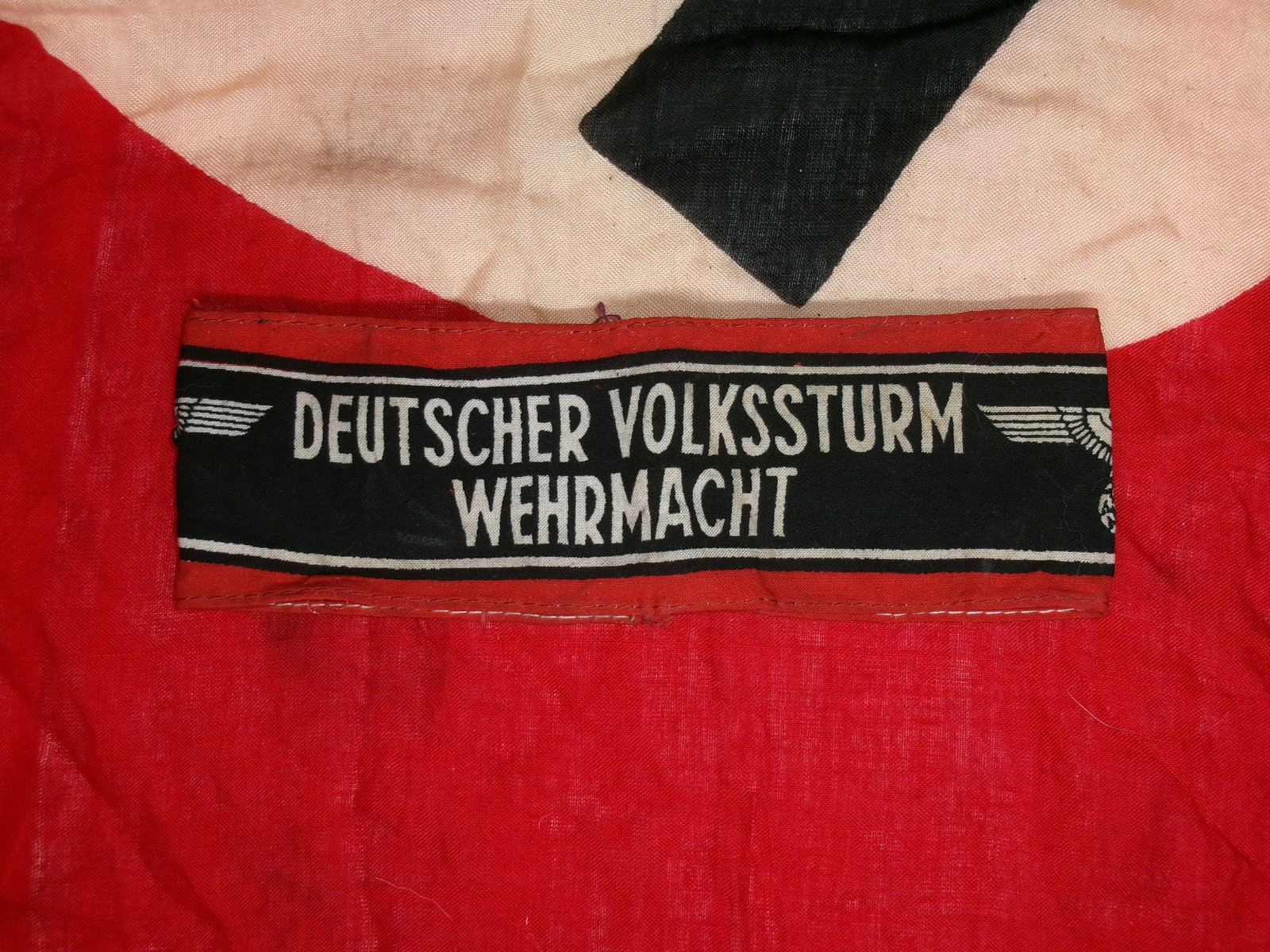 WWII German Volkssturm Armband (“Deutscher Volkssturm Wehrmacht??): A late-war armband issued to members of the Volkssturm, Germany’s militia formed in 1944 as Allied forces advanced into the Reich. The black band with white lettering, bordered in red, identified ir