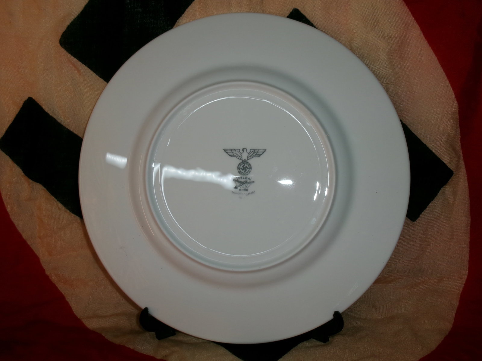 WWII German Porcelain Plate with Reich Eagle Mark (Rhenish Manufacturer): The underside of this white porcelain plate bears a maker’s mark featuring the Reich eagle clutching a swastika above the inscription “Rhenania” and “RWM,” indicating production for 
