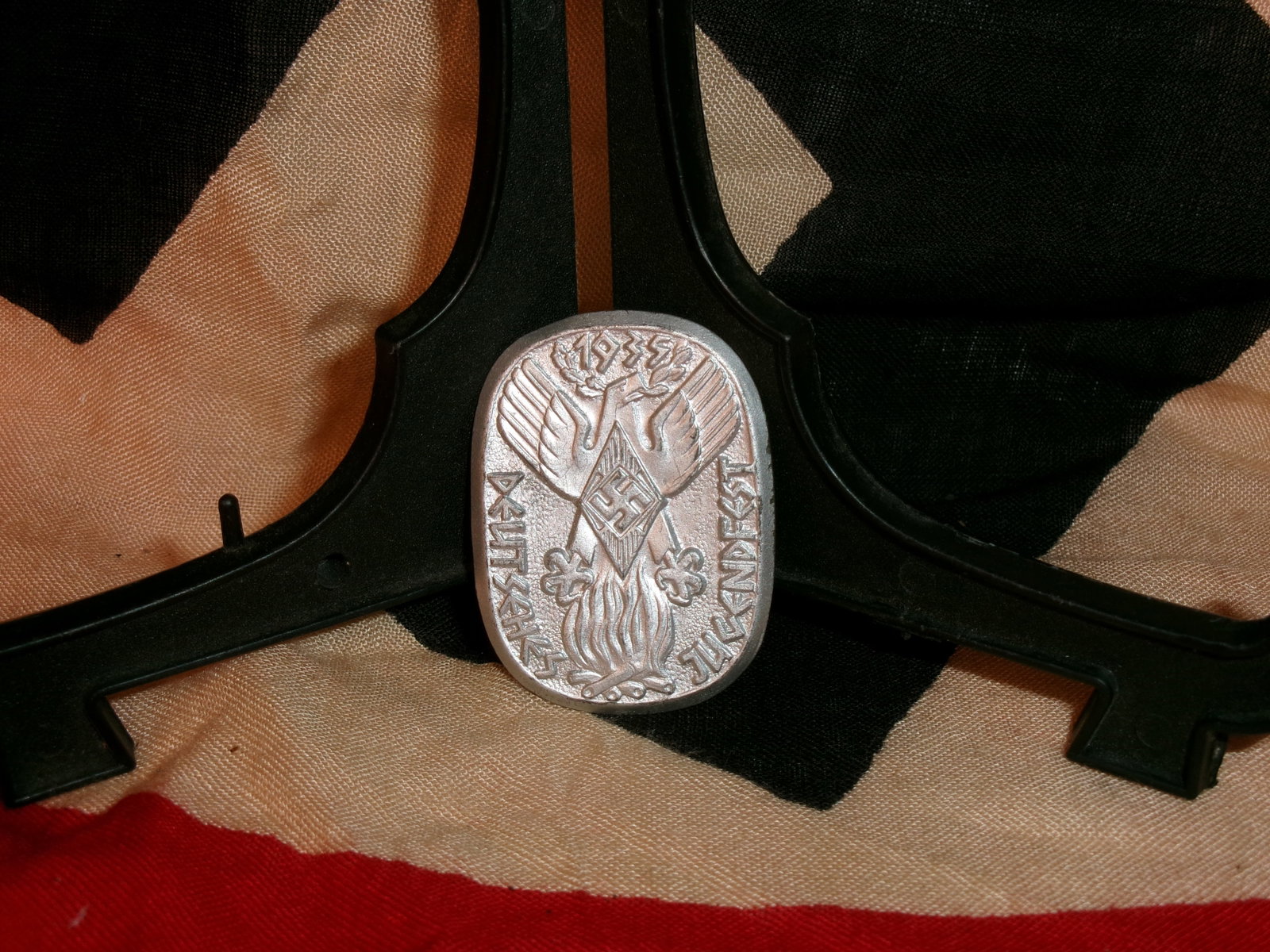WWII-Era German 1935 Deutsches Jugendfest Commemorative Tinnie Badge: This lightweight stamped badge depicts an eagle above a swastika over a stylized flame, surrounded by text referencing the 1935 Deutsches Jugendfest (German Youth Festival). The reverse pin indicates 