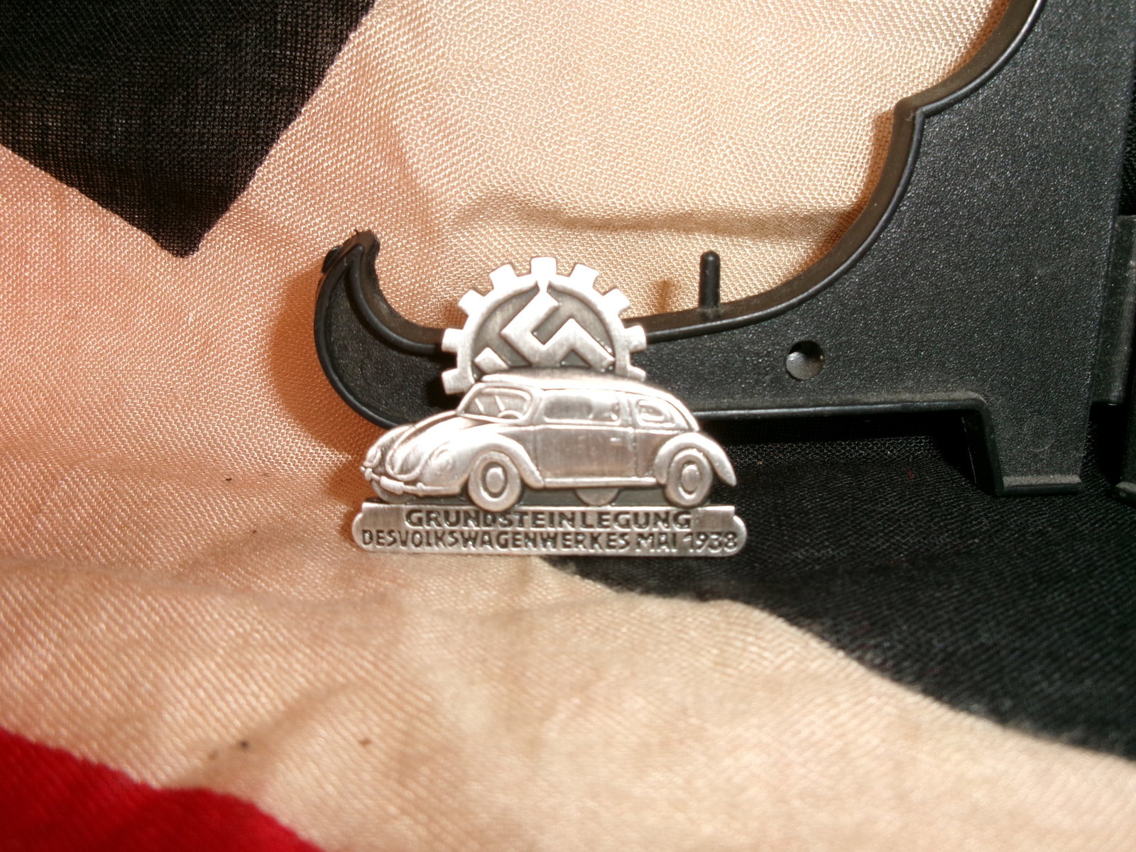 WWII German Volkswagenwerk Foundation Badge By Ges. Gesch.: This stamped metal badge commemorates the laying of the foundation stone for the Volkswagen factory in May 1938. The design features an early Volkswagen car beneath a cogwheel enclosing a swastika, sy