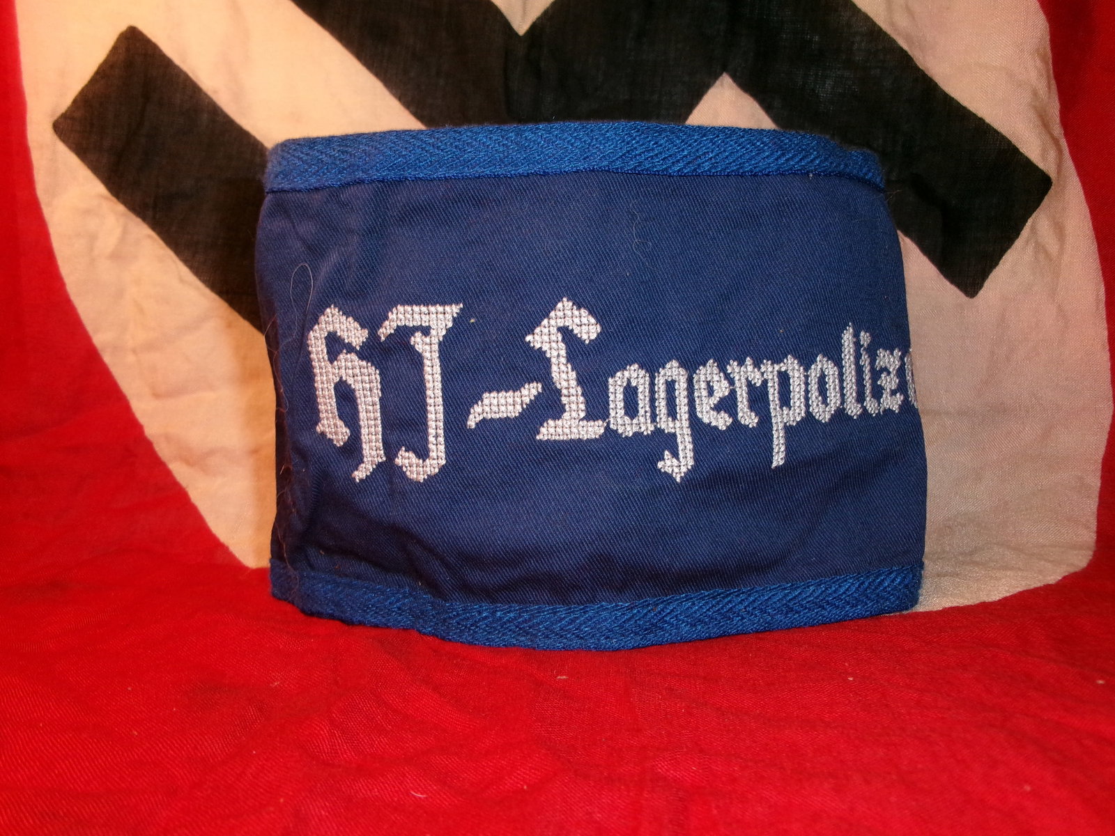 WWII German Hitler Youth Armband (HJ-Lagerpolizei): This blue armband is embroidered with “HJ-Lagerpolizei,” identifying it as worn by members of the Hitler Youth assigned to camp police or supervisory duties. The reverse shows a period tag and