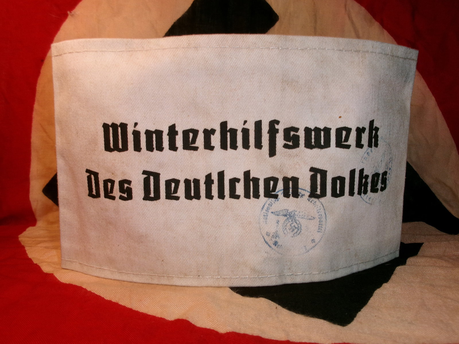 WWII German Winterhilfswerk Armband (Winter Relief Organization Armband): This white cloth armband is printed with the inscription “Winterhilfswerk des Deutschen Volkes” (“Winter Relief of the German People”) in bold black Gothic script. It was worn by volun
