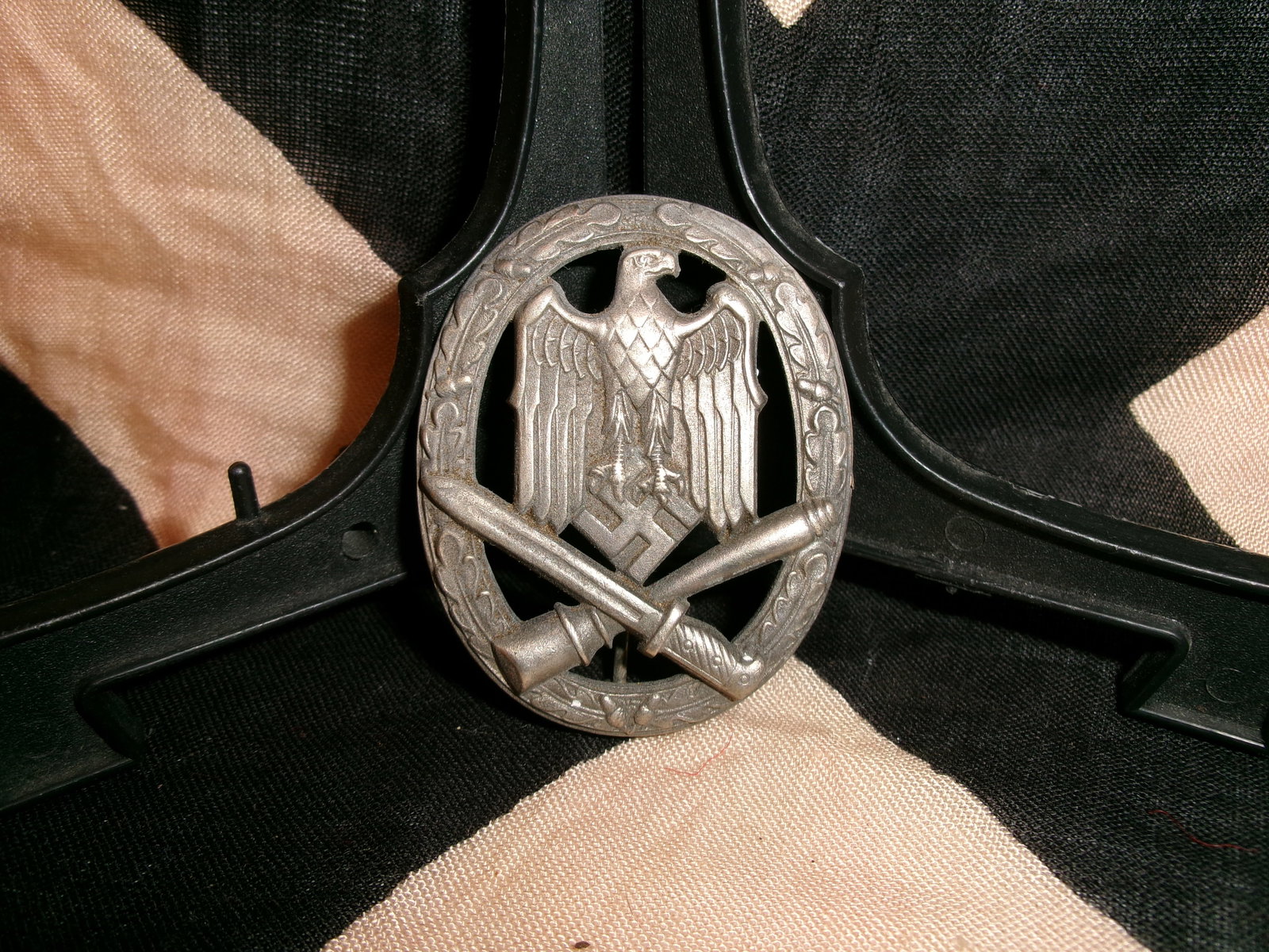 WWII German Infantry Assault Badge (Infanterie-Sturmabzeichen): This oval metal badge depicts a rifle with fixed bayonet crossing diagonally beneath a national eagle, all enclosed within a wreath of oak leaves. The design signifies front-line infantry combat parti