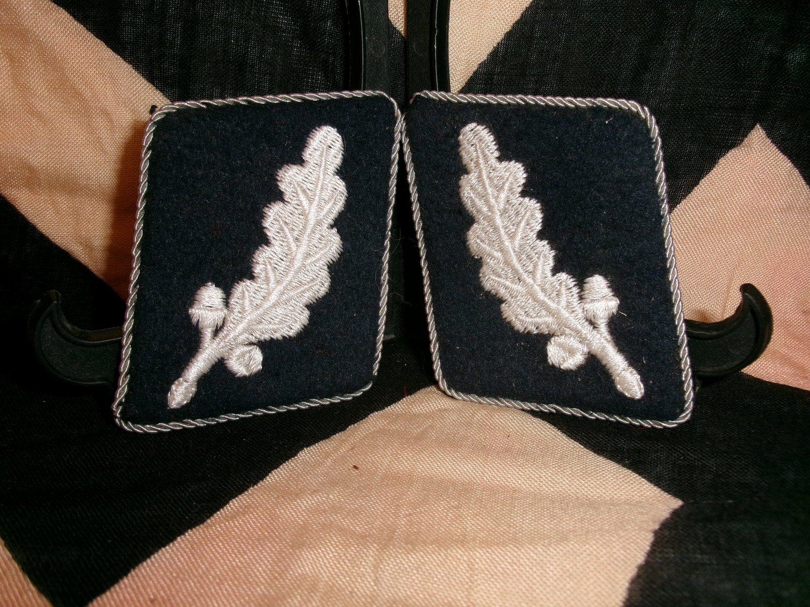 WWII German waffen SS Collar Tabs (Pair): This matched pair of black cloth collar tabs is decorated with embroidered silver oak leaves, framed by twisted silver piping. The oak leaf motif was associated with rank and position within the SS hi