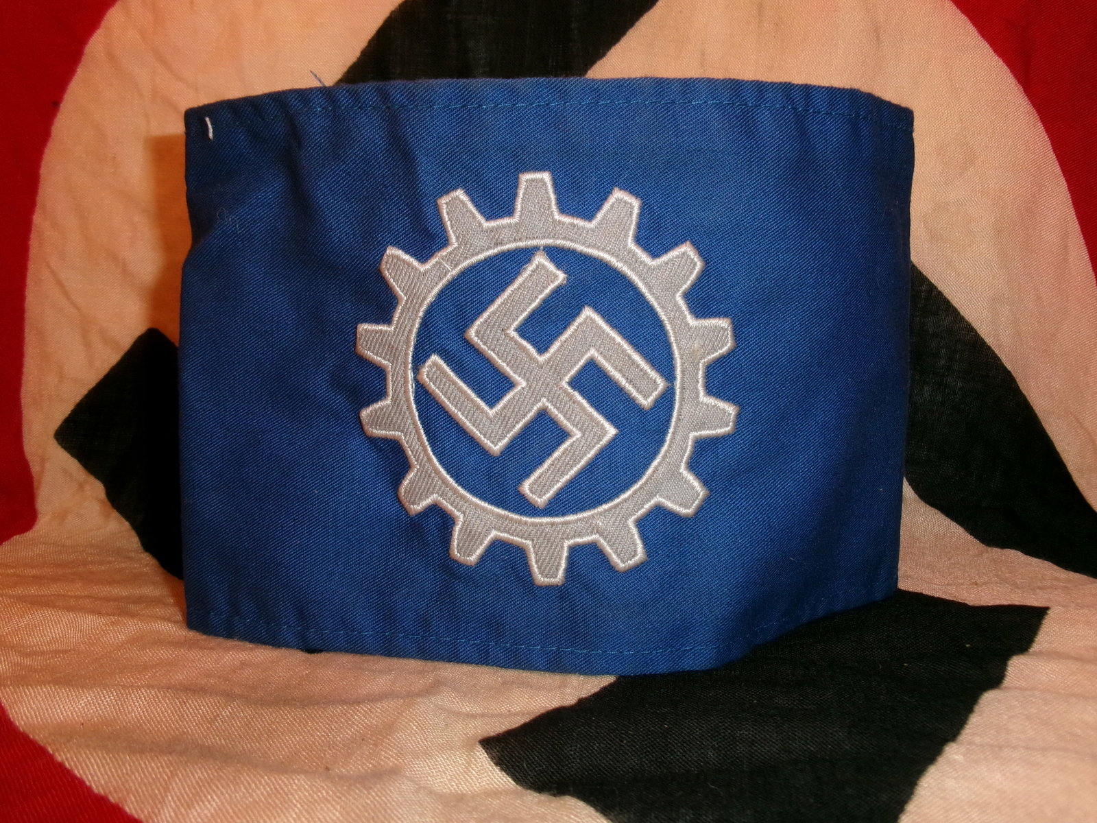 WWII German Industrial Armband (Deutsche Arbeitsfront – DAF With RZM Paper Tag: This blue cloth armband features a white cogwheel encircling a swastika, emblematic of the Deutsche Arbeitsfront (German Labor Front), the state organization that replaced independent trade unions und