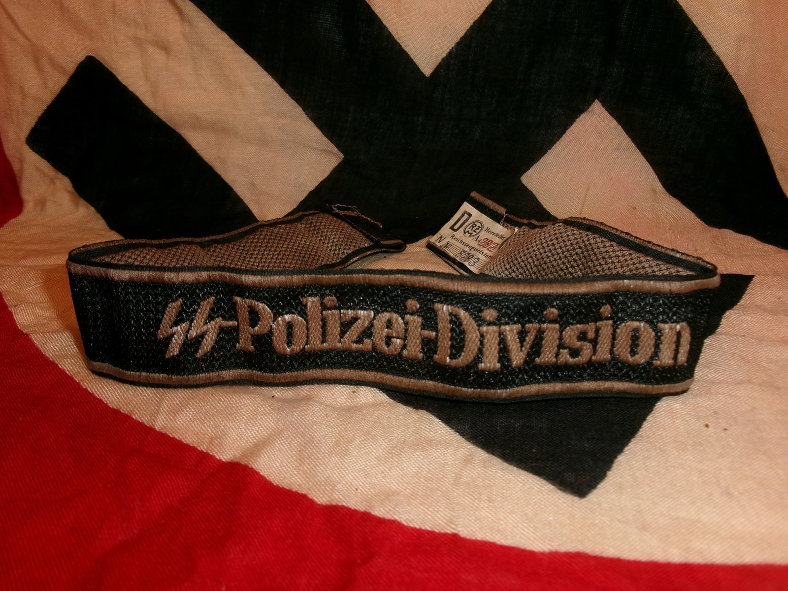 WWII German SS Polizei Division Cuff Title With RZM Paper Tag: This embroidered cuff title bears the inscription “SS-Polizei-Division,” identifying it with the SS Police Division, a unit formed from Ordnungspolizei personnel and integrated into Waffen-SS 
