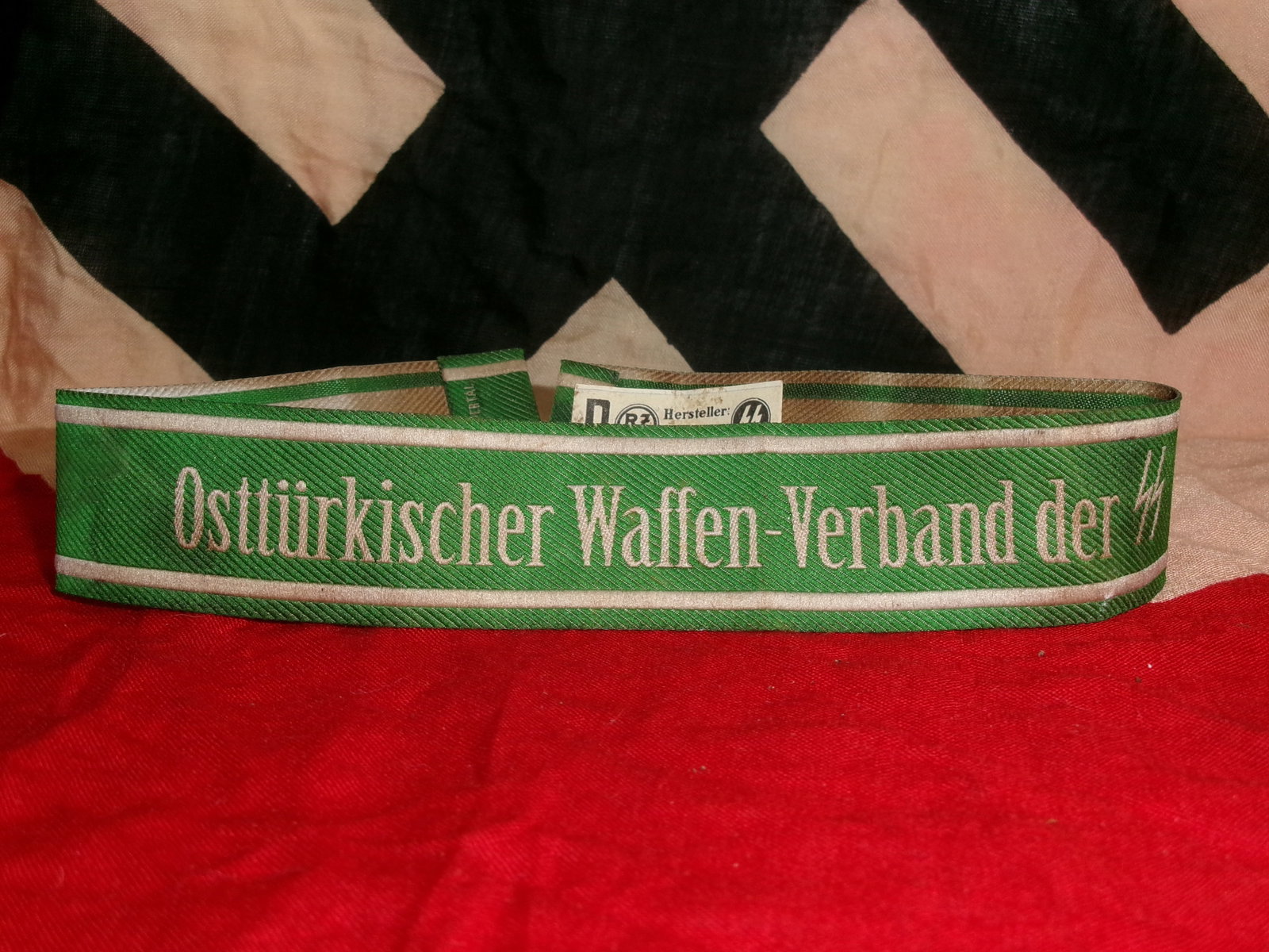 WWII German Volunteer Formation Cuff Title – “Osttürkischer Waffen-Verband der SS?? With RZM: This woven cuff title, in green with silver-gray script, reads “Osttürkischer Waffen-Verband der SS,” identifying a formation composed of Eastern Turkic volunteers incorporated into German fo