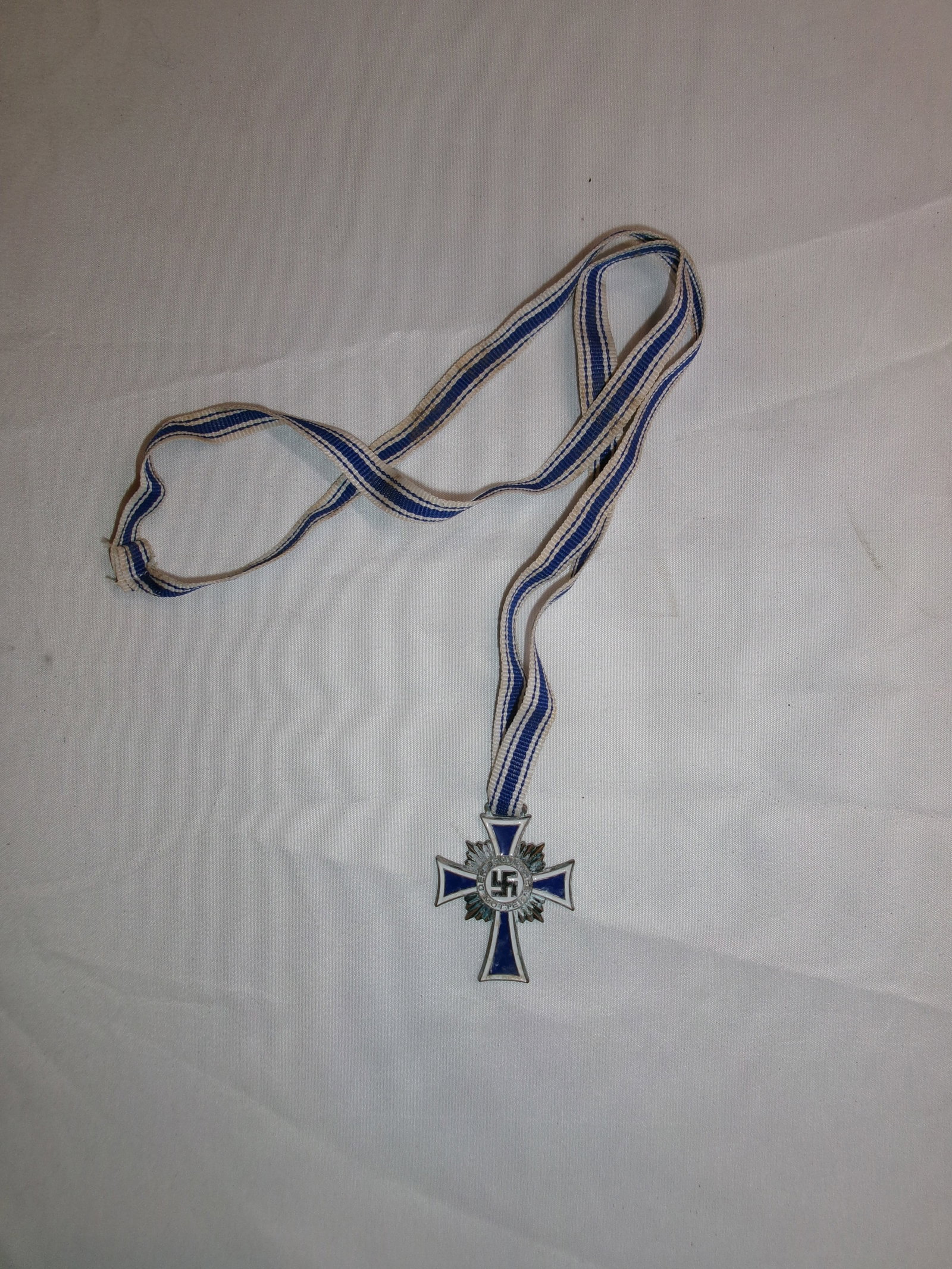 WWII German Mother’s Cross (Ehrenkreuz der Deutschen Mutter) with Ribbon: A German Mother’s Cross (Ehrenkreuz der Deutschen Mutter), awarded during the Third Reich to recognize mothers for large families in support of state population policies. The decoration consists of 