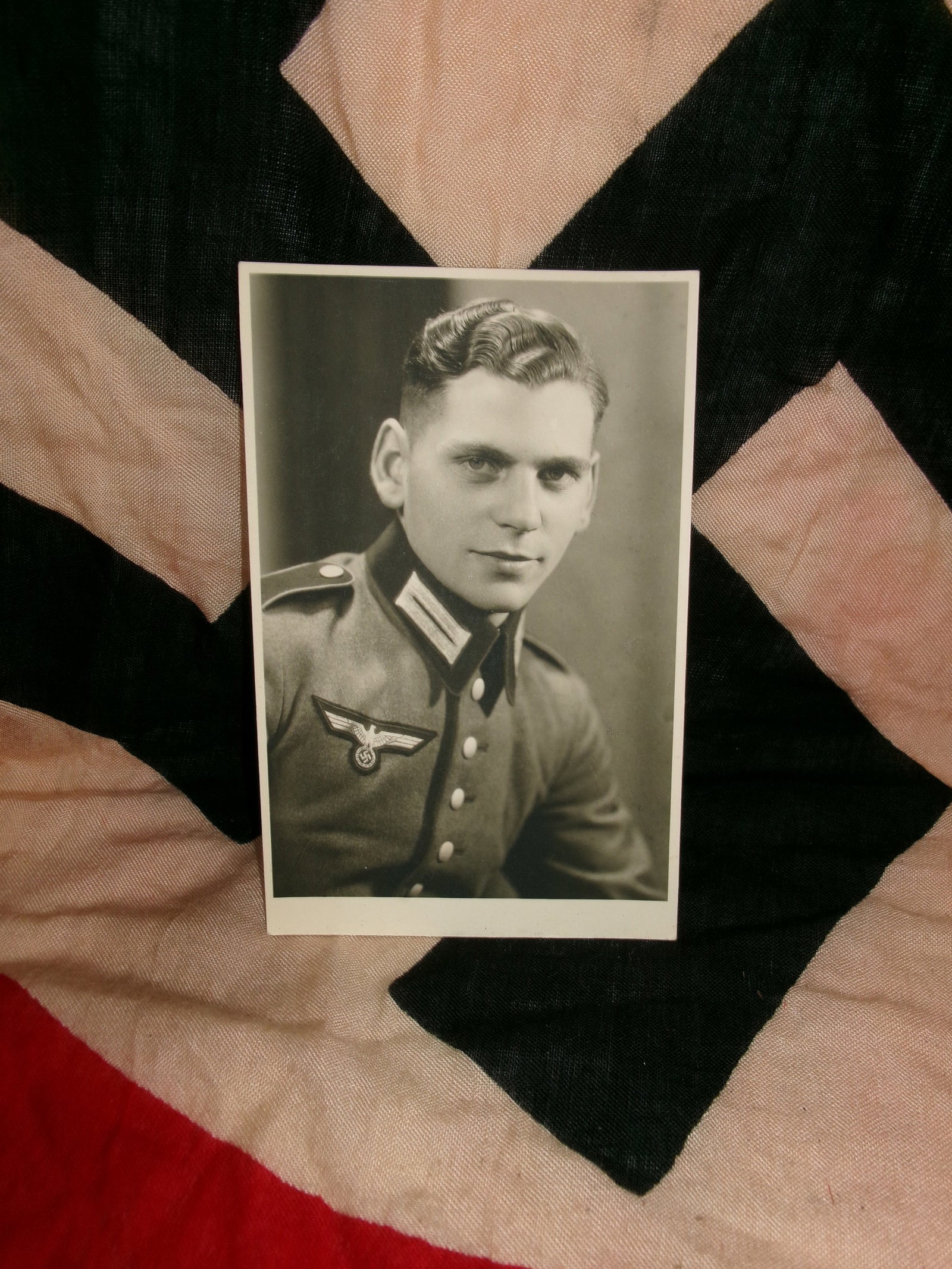 WWII German Soldier Studio Portrait Photograph: A black-and-white studio portrait of a young German soldier in uniform, captured in formal pose. The subject’s tunic displays period insignia, including a national eagle emblem, indicating affiliati