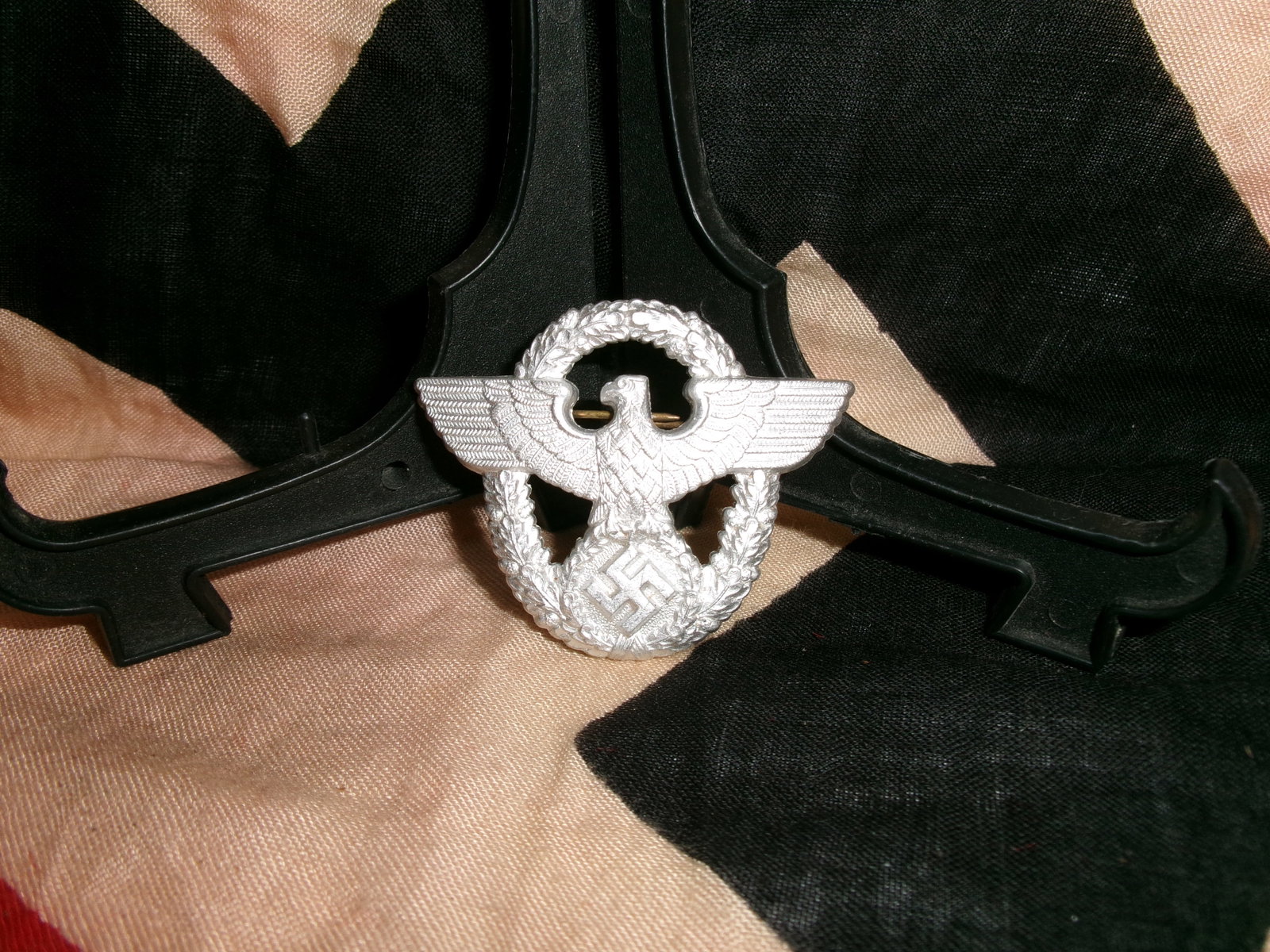 WWII German Police Aluminum Cap Eagle (Polizei Mützenadler): A lightweight aluminum cap badge featuring a spread-wing eagle clutching a wreath enclosing a swastika, characteristic of German police insignia during the Second World War. Designed for wear on servi