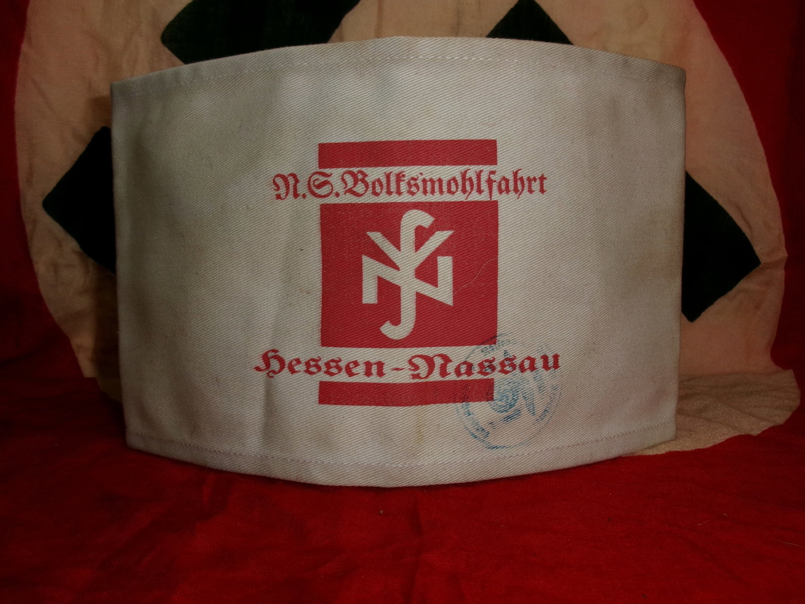 WWII NS-Volkswohlfahrt Hessen-Nassau Armband: A white cloth armband printed in red with “N.S. Volkswohlfahrt Hessen-Nassau,” identifying the National Socialist People’s Welfare organization and its regional branch. This organization coo