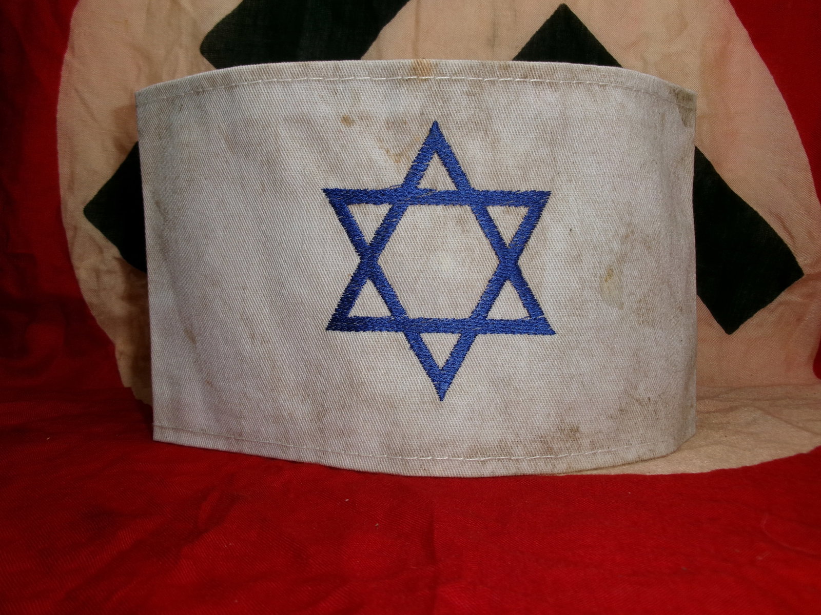 WWII Jewish Identification Armband with Star of David: A white cloth armband bearing a blue Star of David, associated with the enforced identification of Jewish individuals under Nazi rule during the Second World War. The simple cotton construction and bo