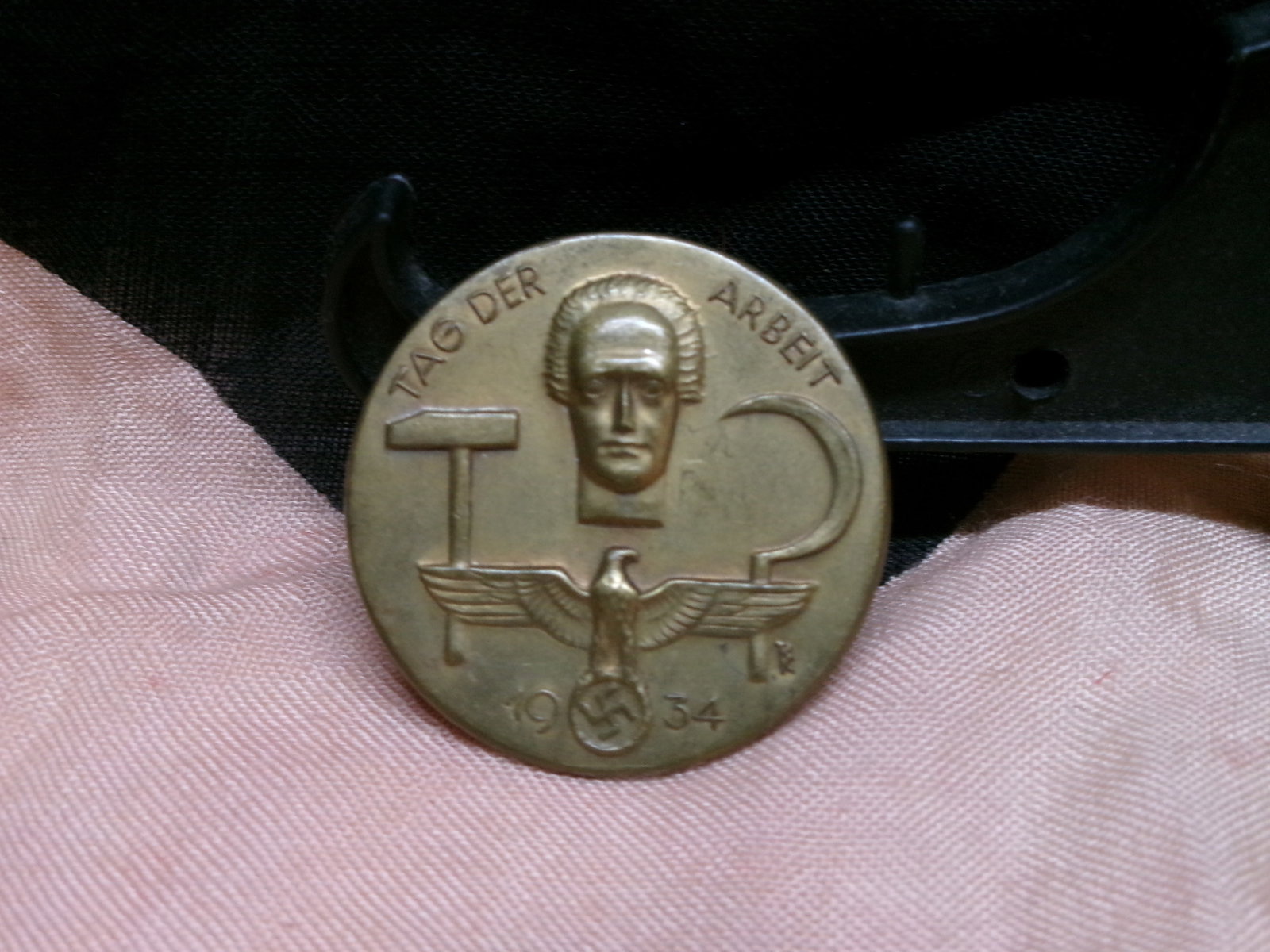 WWII German “Tag der Arbeit?? Commemorative Badge (Labor Day Tinnie, 1934): A circular commemorative badge issued for the 1934 “Tag der Arbeit” celebration, incorporating imagery of a worker’s head, tools symbolizing labor, and a national eagle with swastika. These 