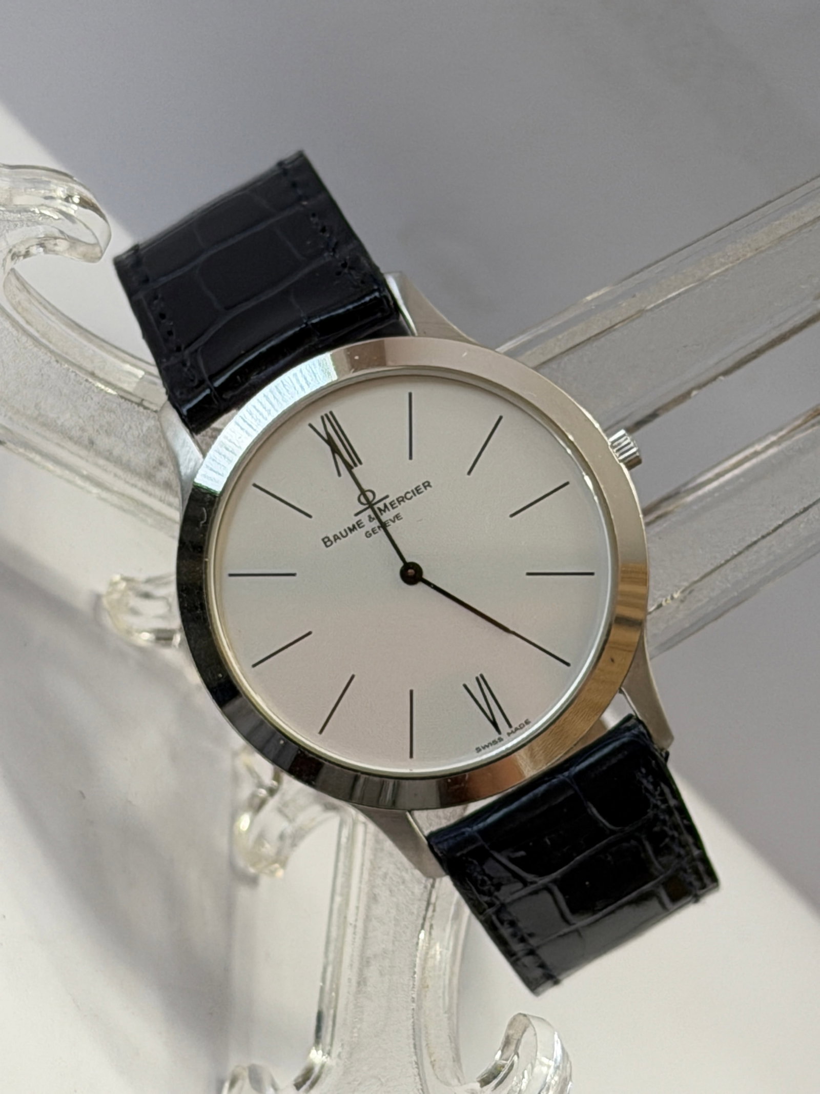 Baume & Mercier Men’s Dress Watch – Swiss Made – Stainless Steel – Leather Strap: Elegant Baume & Mercier men’s dress watch featuring a clean, minimalist silver-tone dial with slim hour markers and Roman numerals at 12 and 6. Classic Swiss design with a polished stainless steel c