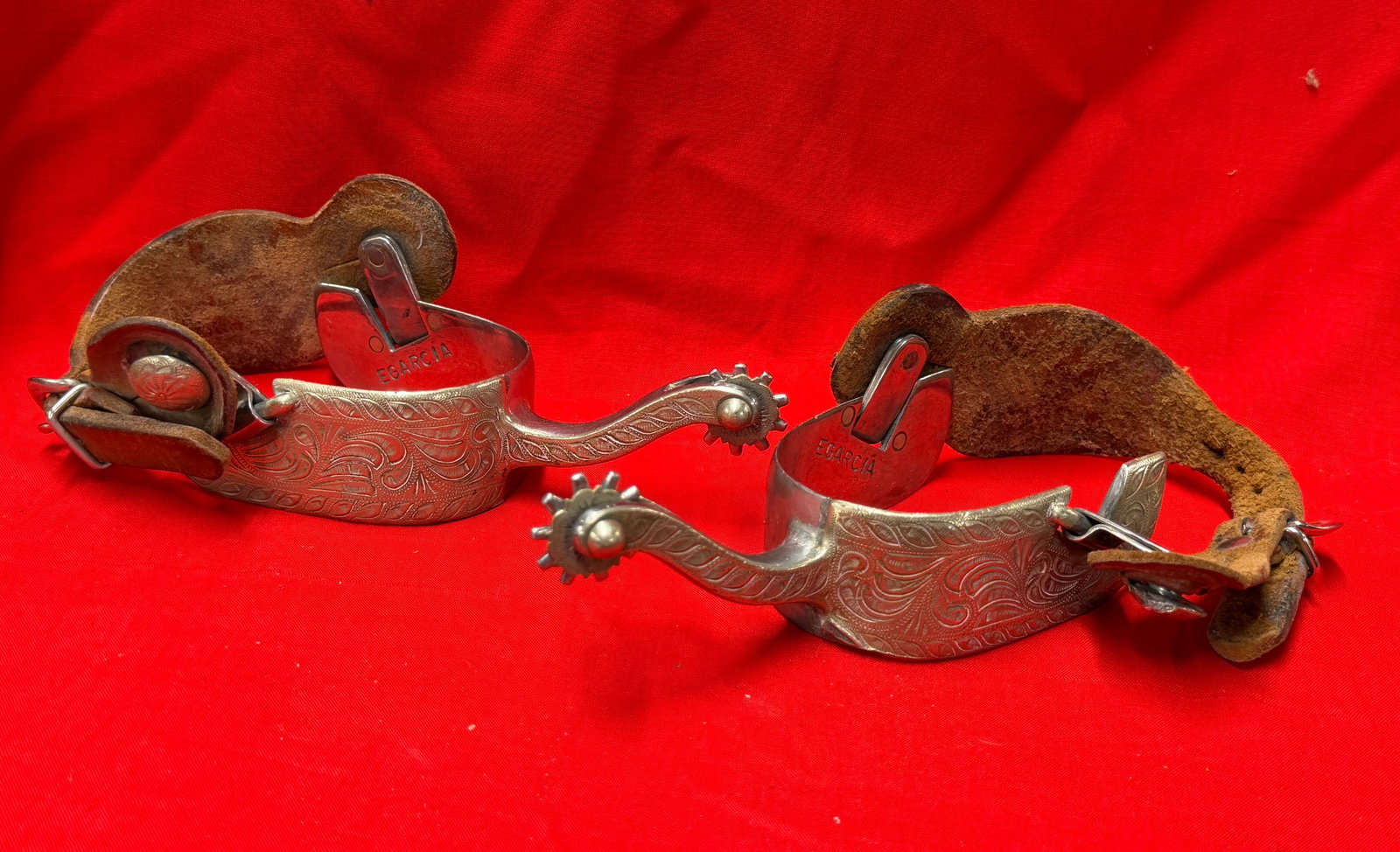 Vintage E Garcia Hand Engraved Western Cowboy Spurs With Leather Straps Pair: Pair of vintage western cowboy spurs marked EGARCIA featuring detailed hand engraved floral scrollwork throughout the heel bands and shanks. Includes attached aged leather spur straps with decorative 